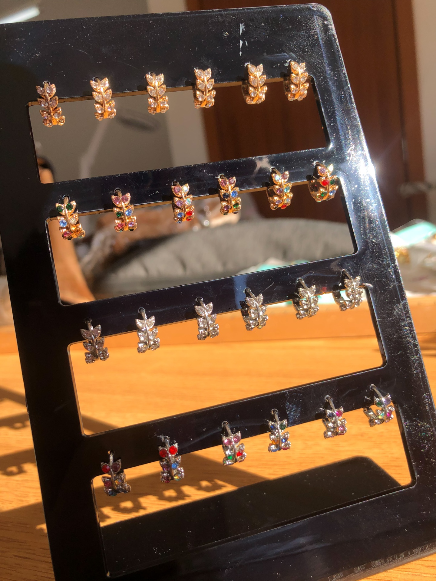 Expositor preto com 20 pares de brincos pequenos em metal dourado e prateado com pedras coloridas.