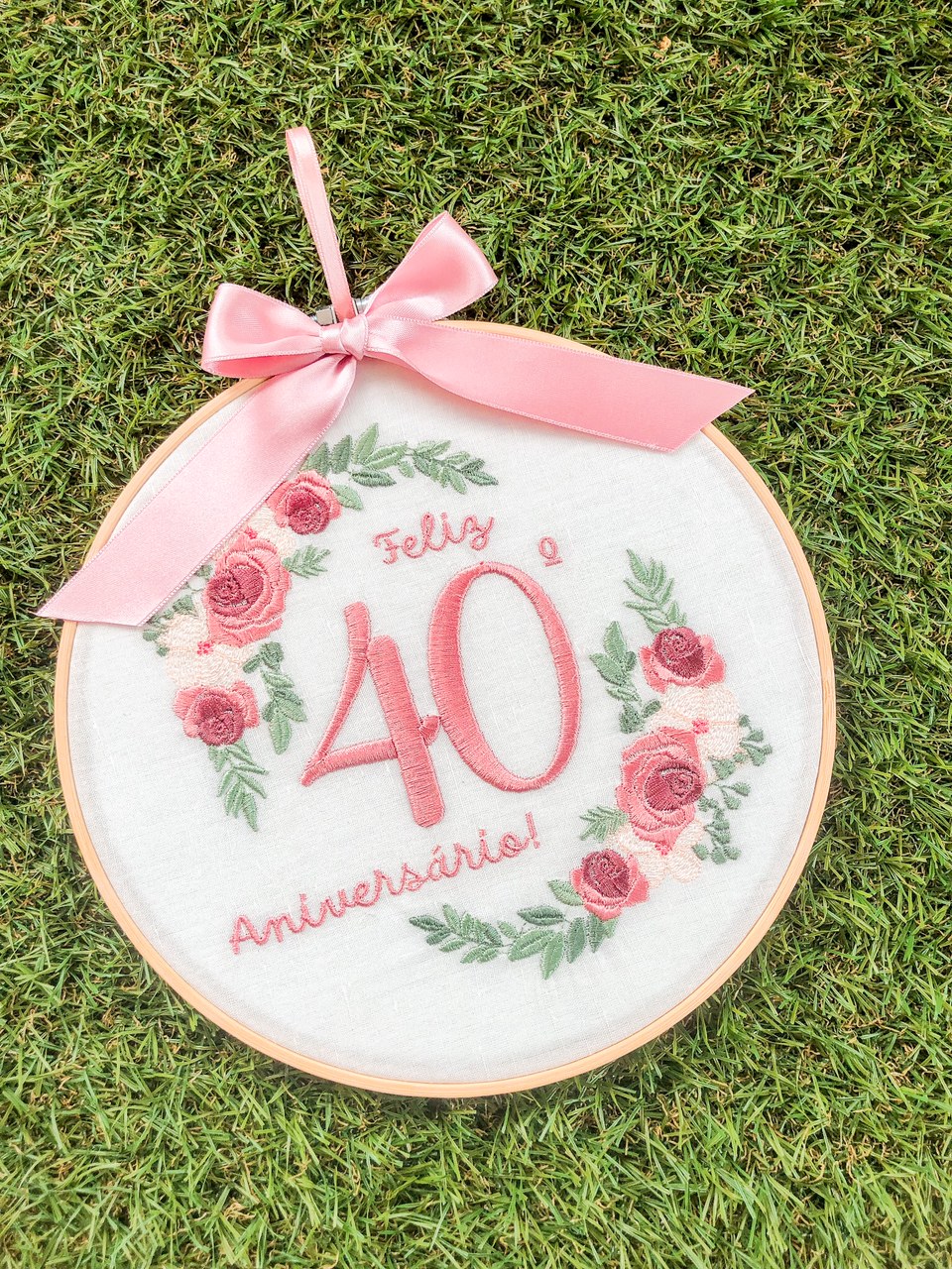 Aro de bordado com texto e decoração floral sobre relva