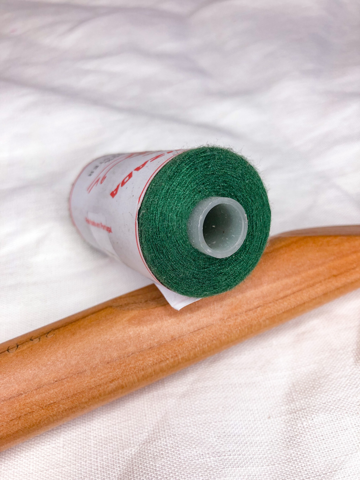 Rolo de linha verde com rótulo branco e vermelho, fita cola castanha, sobre tecido branco