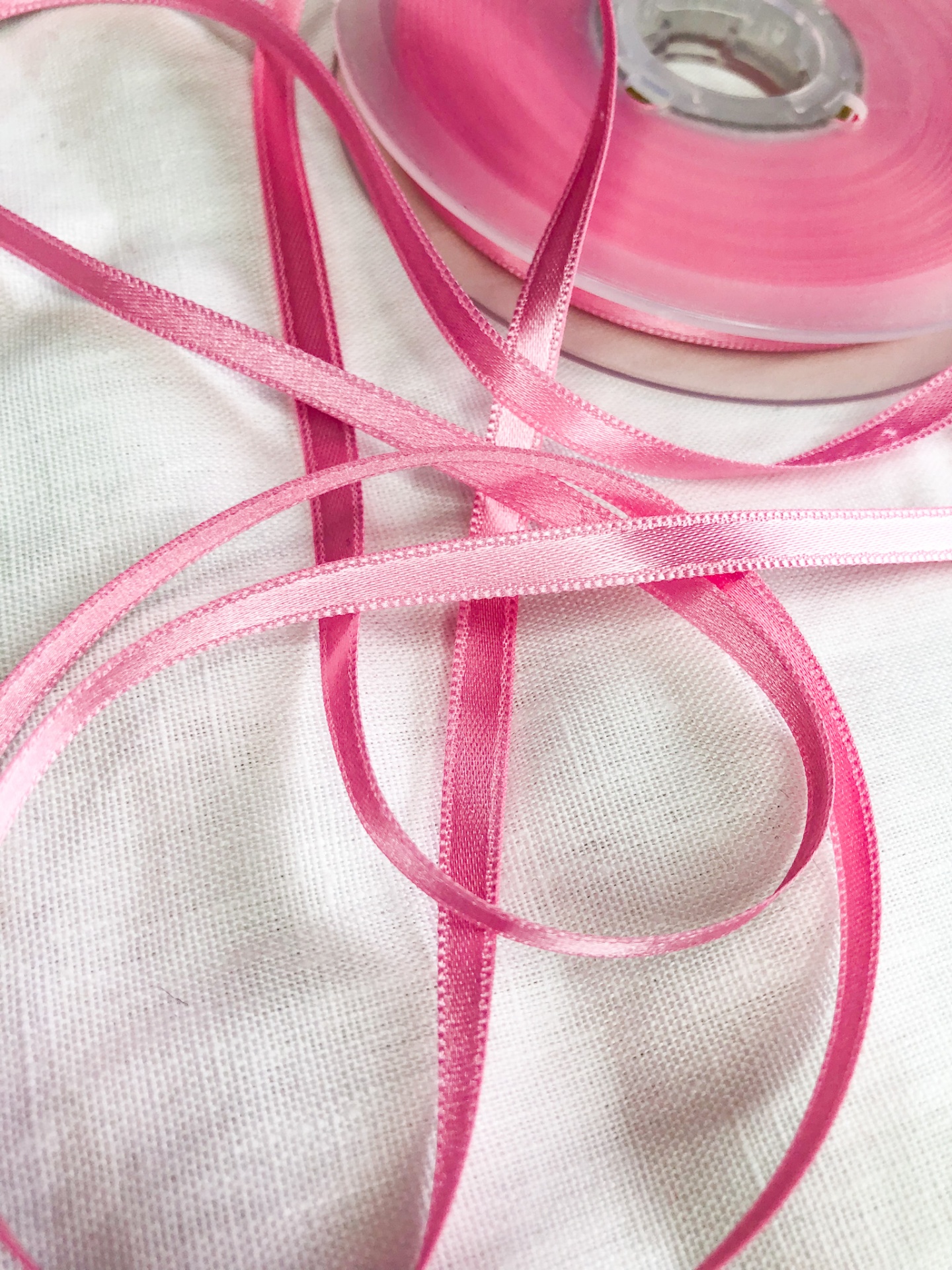 Fita de cetim rosa fina enrolada em bobina sobre tecido branco