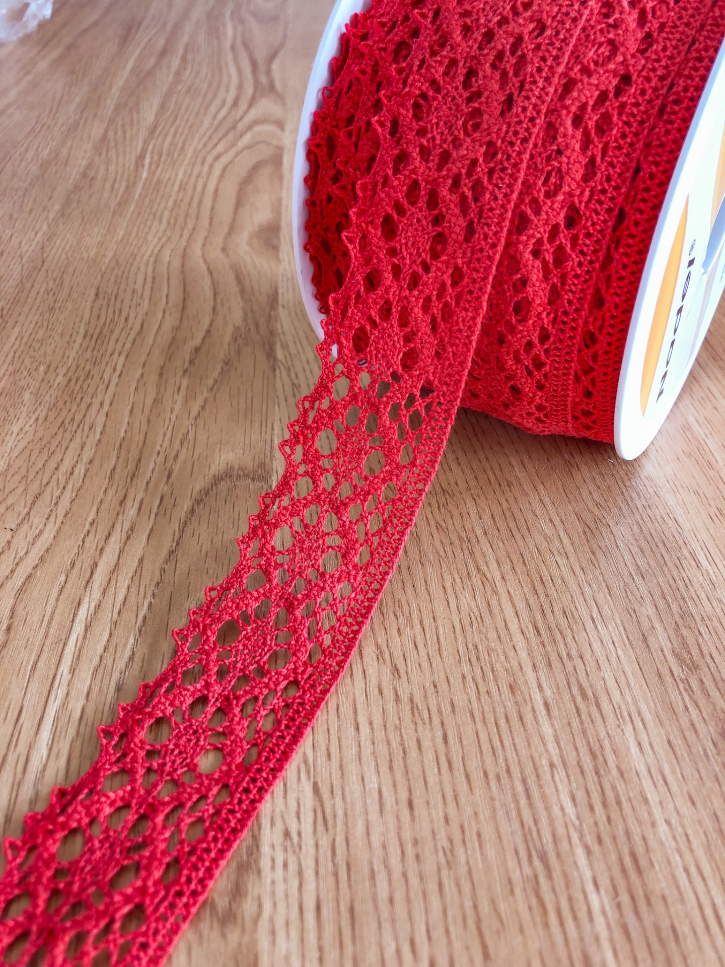 Rolo de fita de renda vermelha com padrão entrelaçado sobre madeira