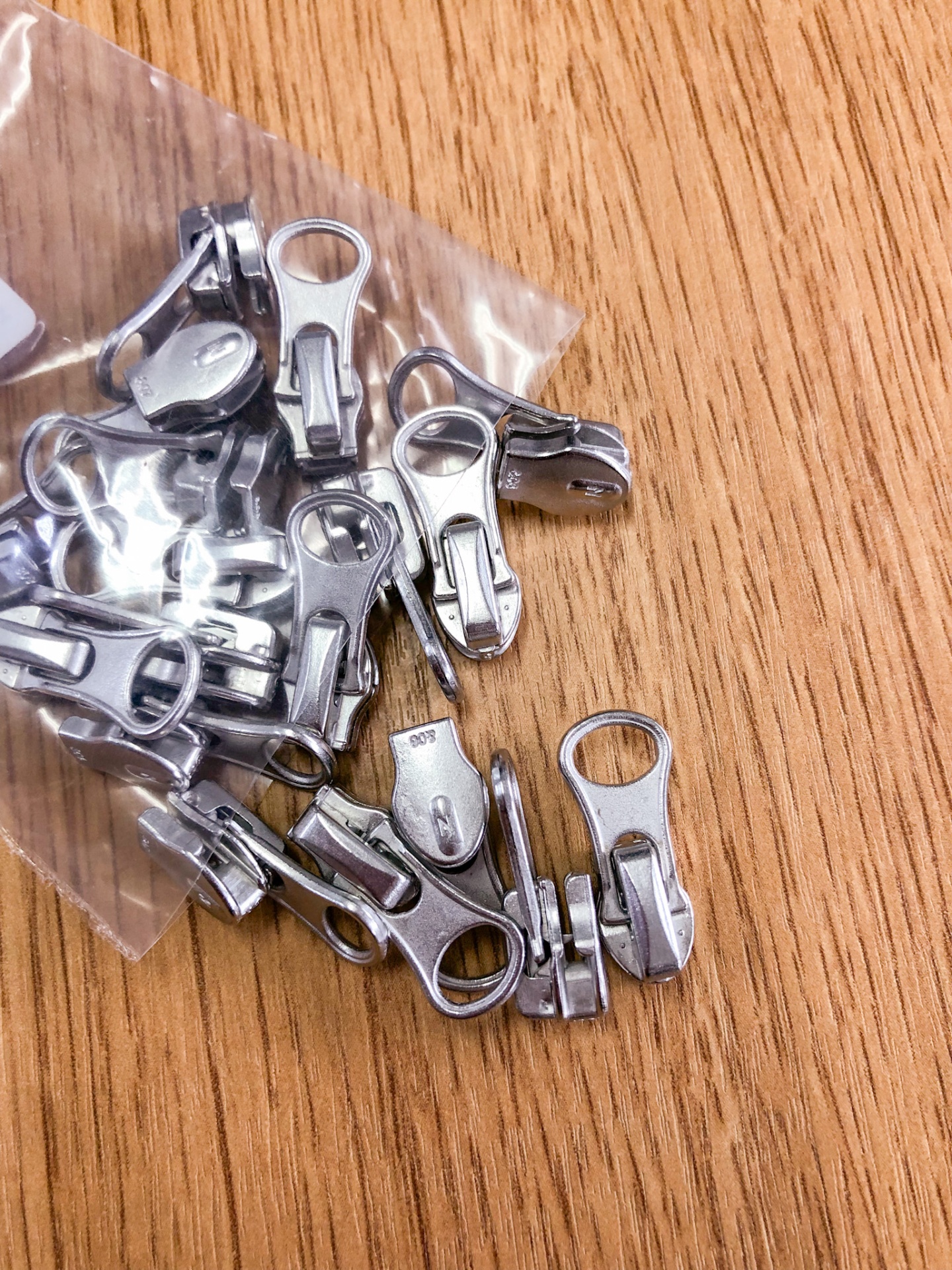 Puxadores metálicos para fecho éclair prateados sobre madeira clara