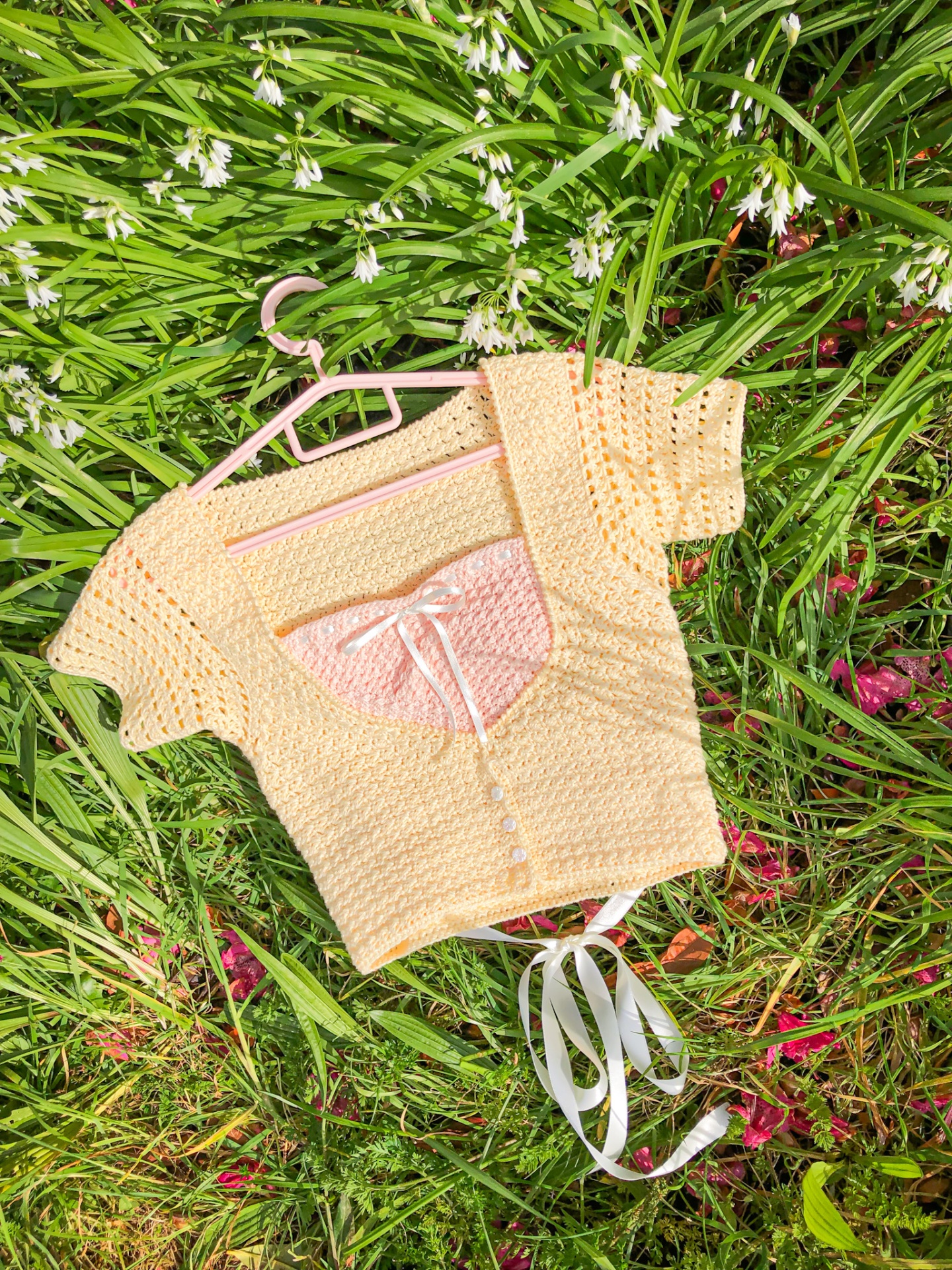 Camisola de malha bege em cabide sobre relva com flores