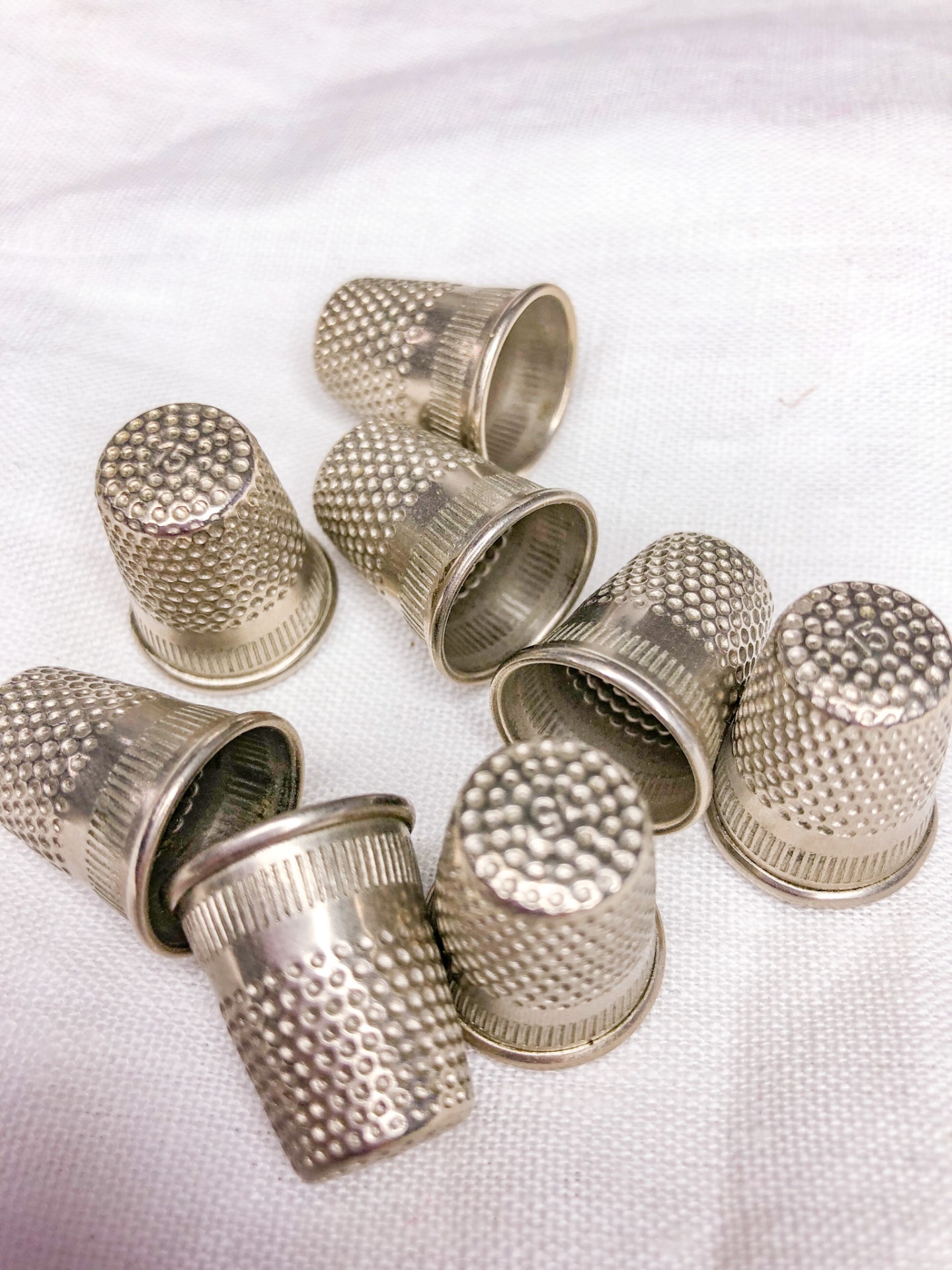 Oito dedais metálicos prateados com textura em relevo sobre tecido branco