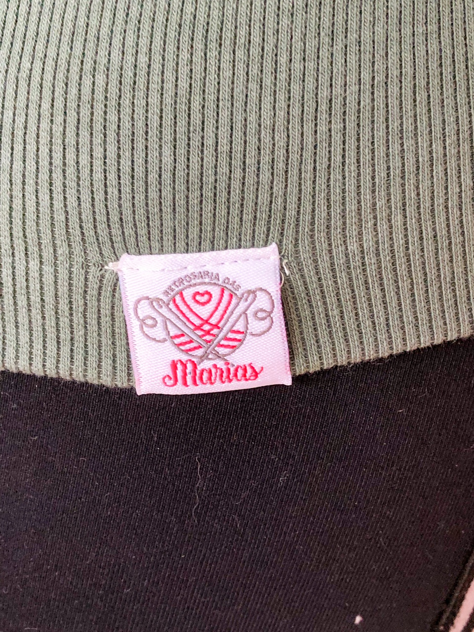 Etiqueta rosa bordada com texto ARTESANARIA DAS MARIAS em tecido verde e preto