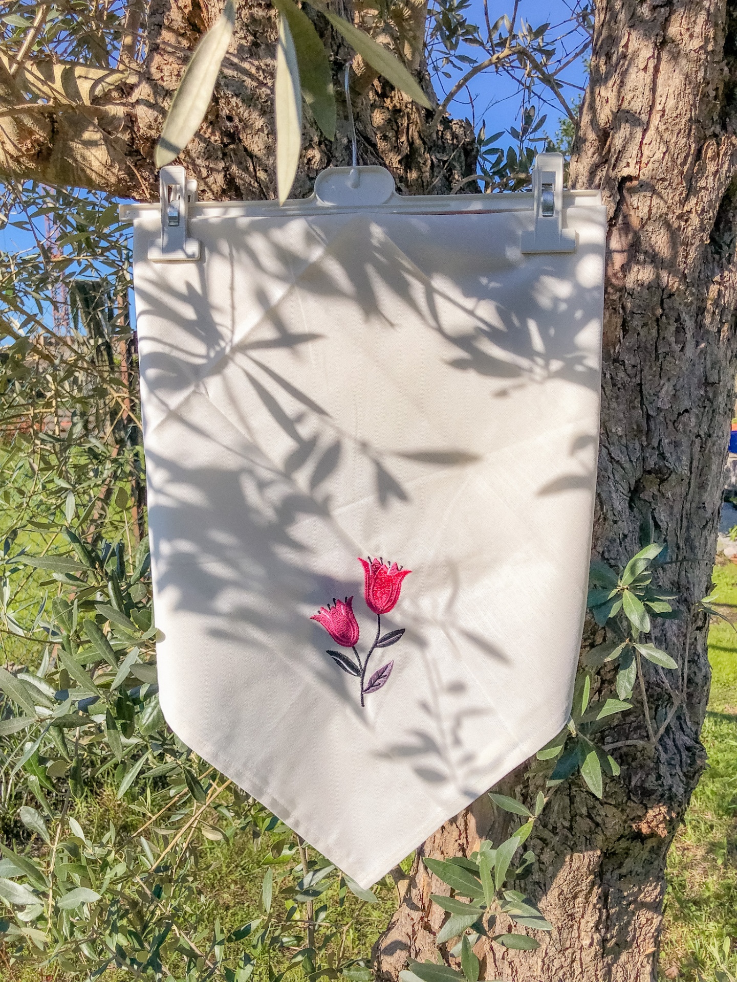 Pano branco com bordado de flores cor-de-rosa pendurado numa árvore