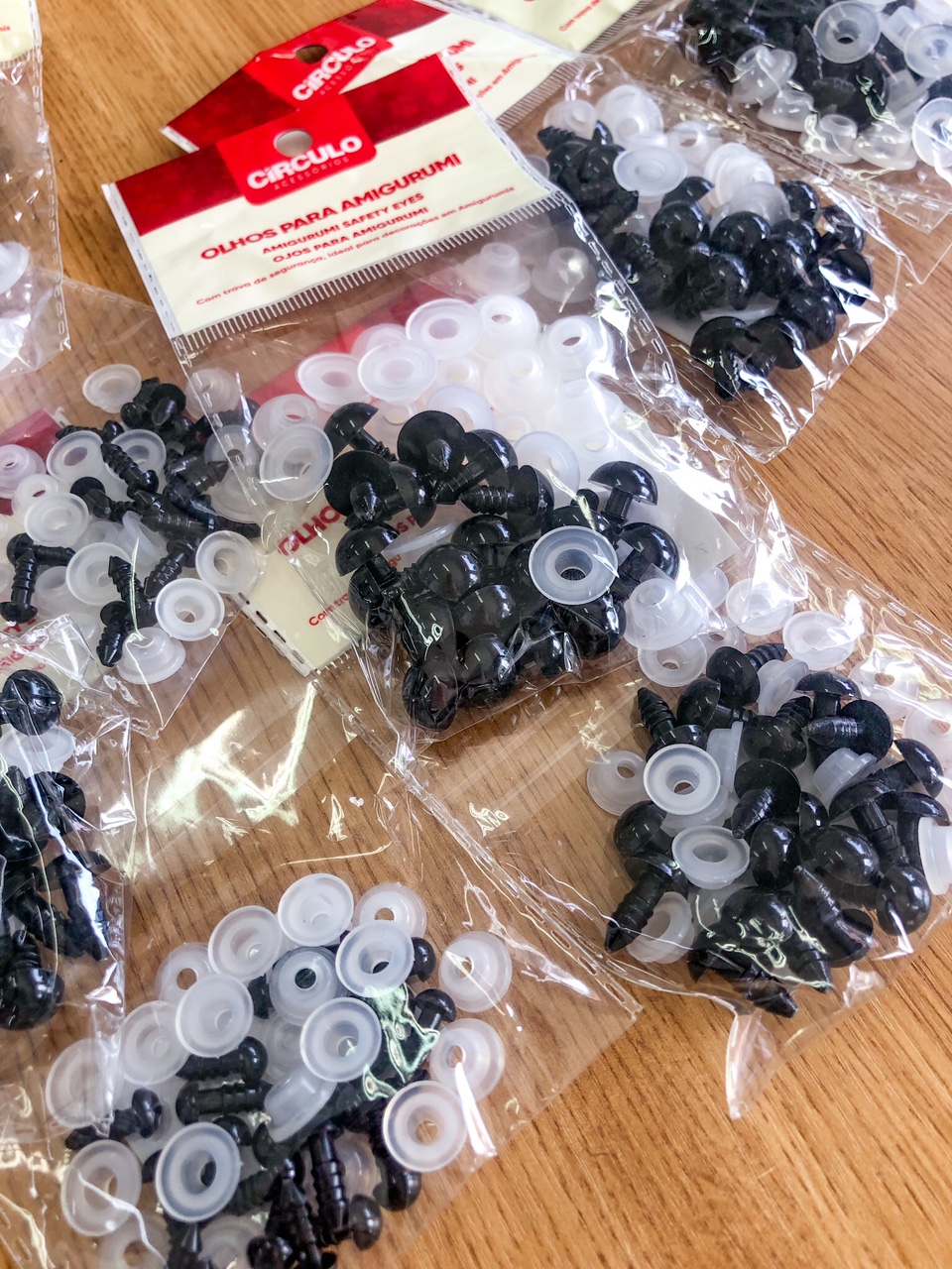 Pacotes de olhos de plástico para amigurumi Circulo em sacos transparentes sobre mesa de madeira