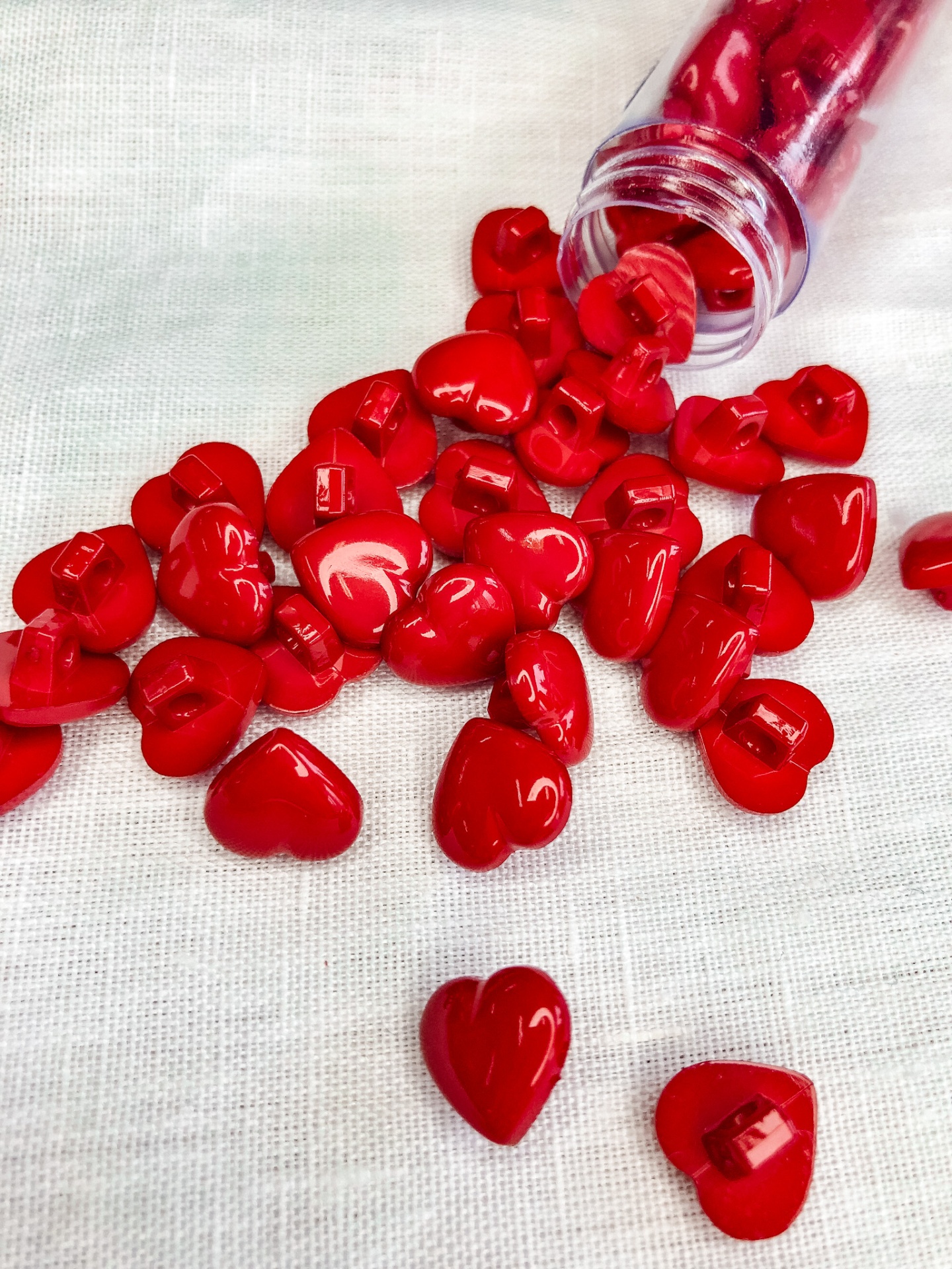 Contas vermelhas em forma de coração espalhadas sobre tecido branco com frasco transparente