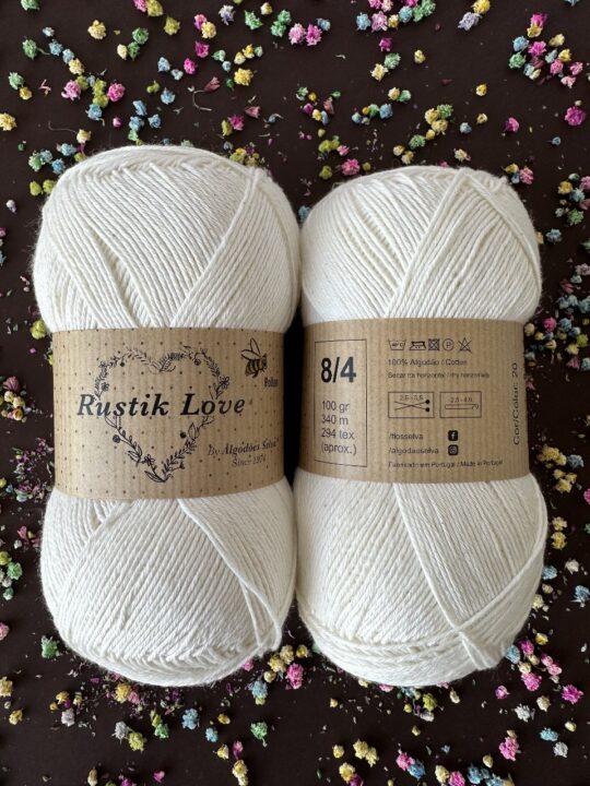 Dois novelos de lã branca Rustik Love com etiquetas castanhas e texto visível sobre composição e cuidados.