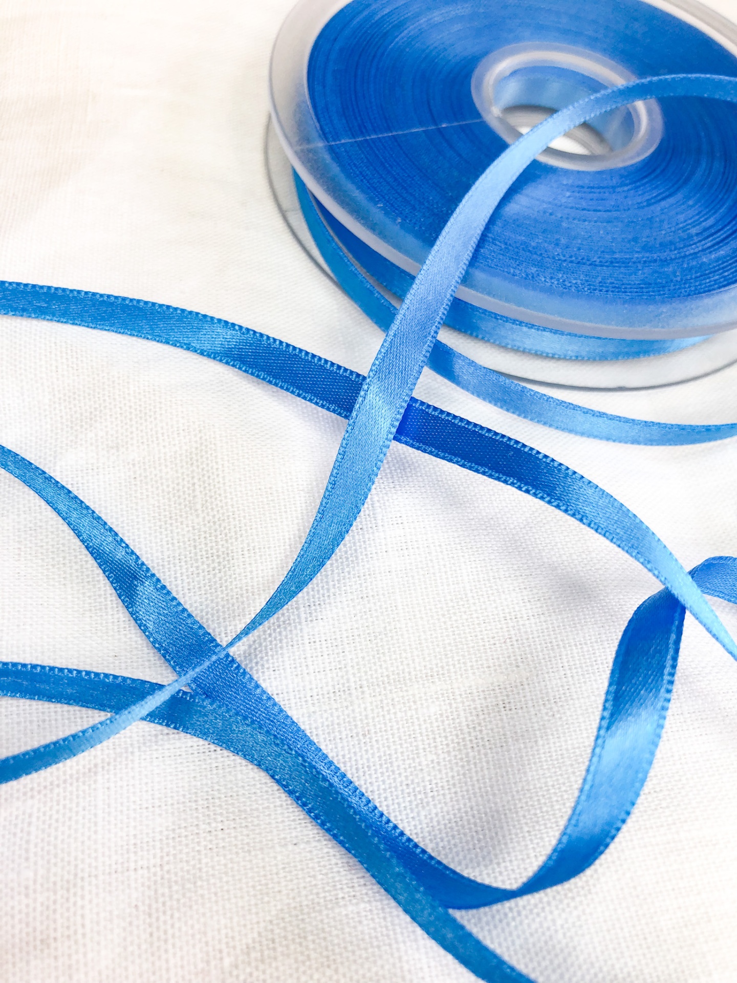 Fita de cetim azul em bobina sobre tecido branco
