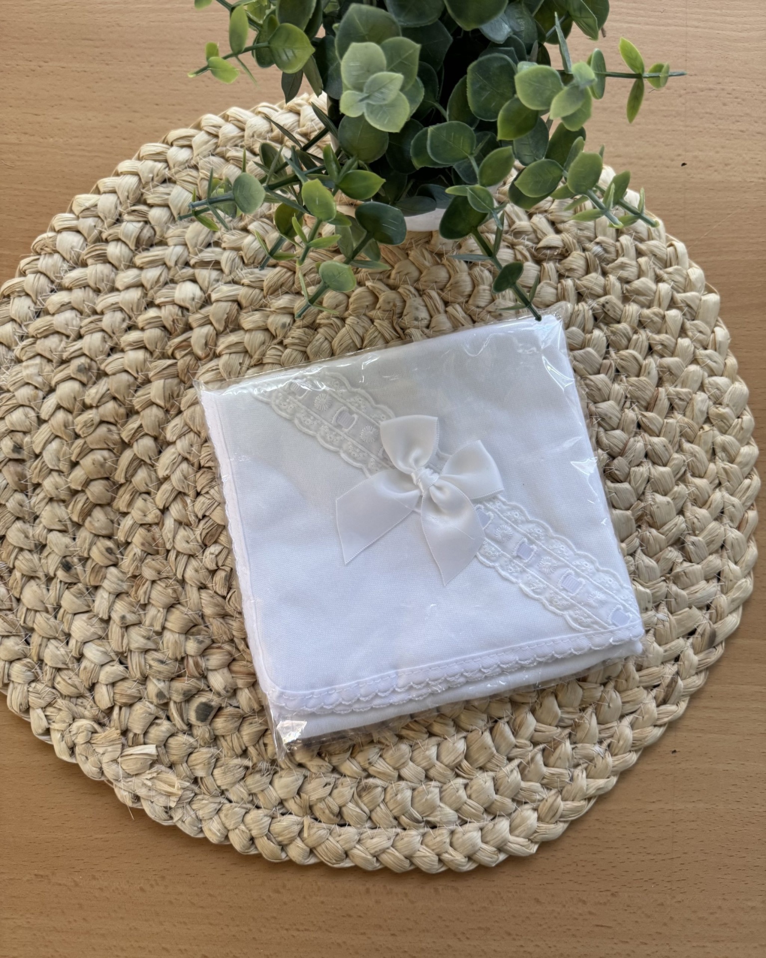 Guardanapo branco com renda e laço sobre suporte trançado com planta verde