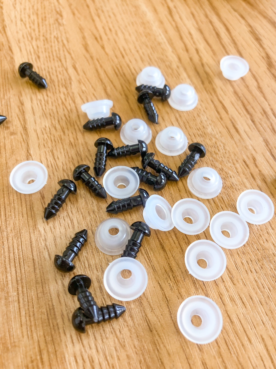 Pequenos parafusos pretos e buchas plásticas brancas sobre madeira clara