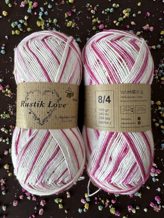 Duas meadas de fio de algodão branco e rosa com etiquetas Rustik Love e informações de peso e composição
