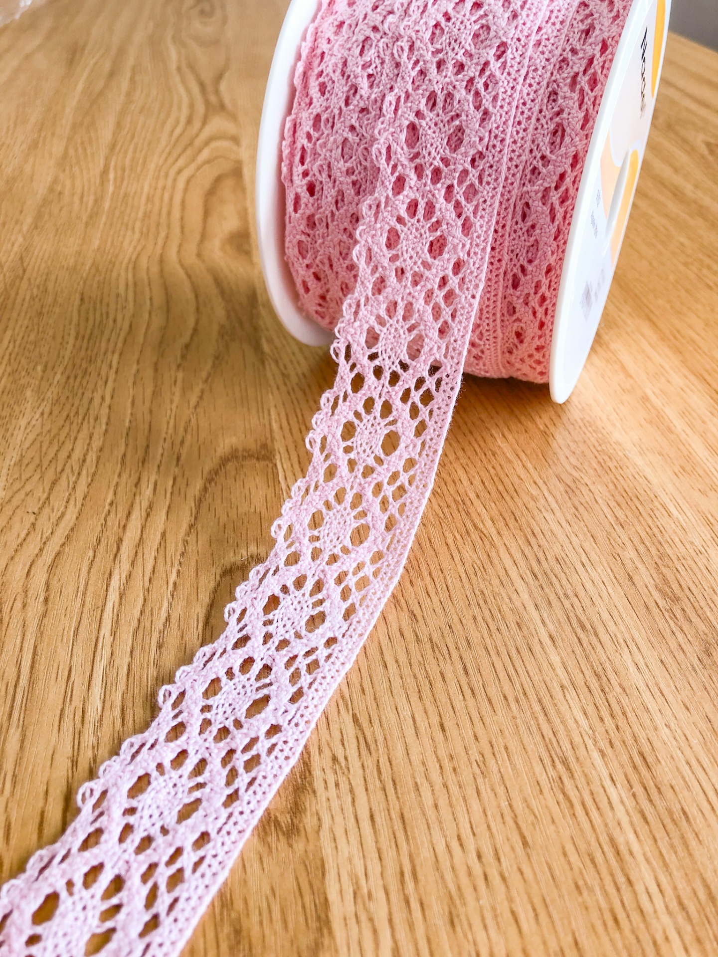Rolo de renda cor-de-rosa claro com padrão aberto colocado em madeira