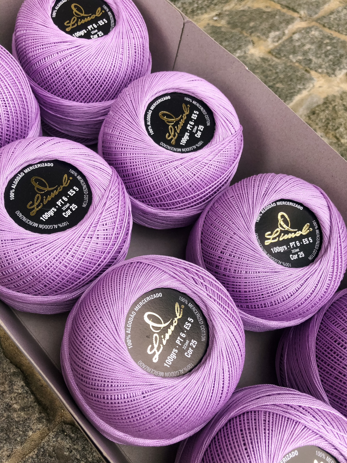 Bolas de linha lilás claro com etiquetas pretas e douradas numa caixa