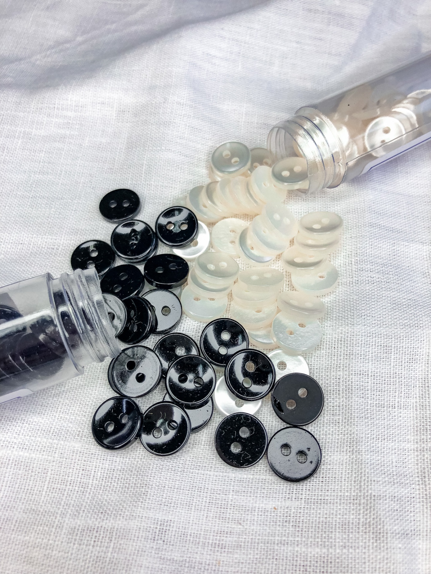 Botões pretos e brancos de plástico com dois furos sobre tecido branco
