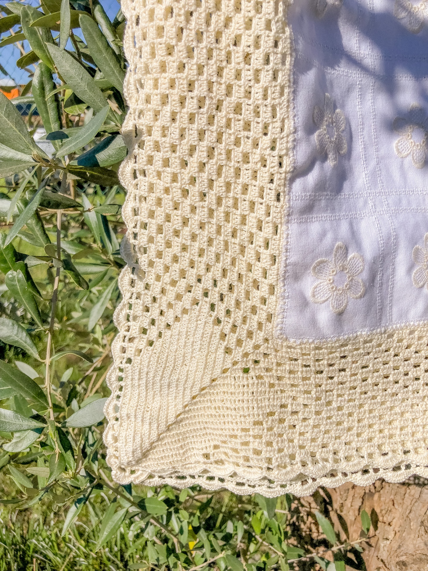Pano branco com bordado floral bege e renda croché amarela sobre tronco de árvore