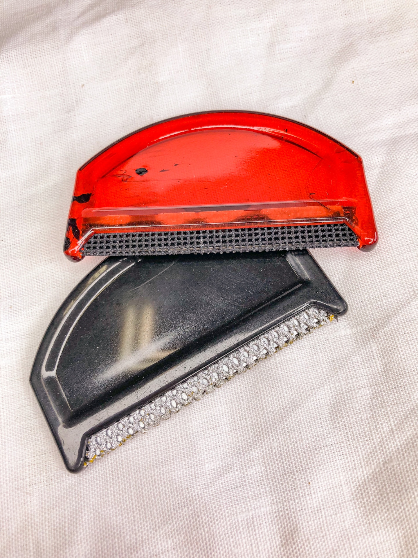 Dois raspadores para gelo, vermelho e preto, sobre tecido claro