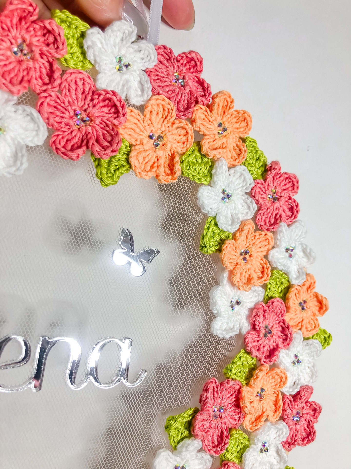 Decoração circular com flores em crochê coloridas e texto prateado num fundo transparente.