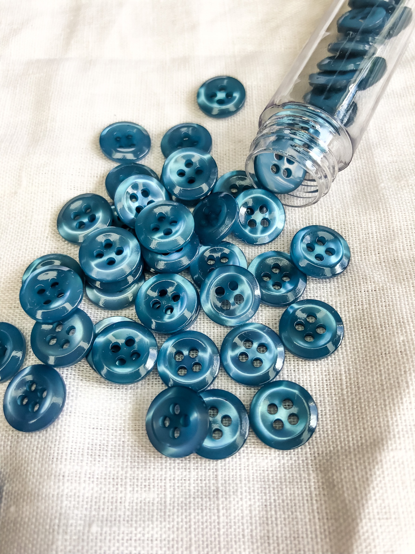 Botões redondos azuis brilhantes com quatro furos sobre tecido claro ao lado de frasco plástico