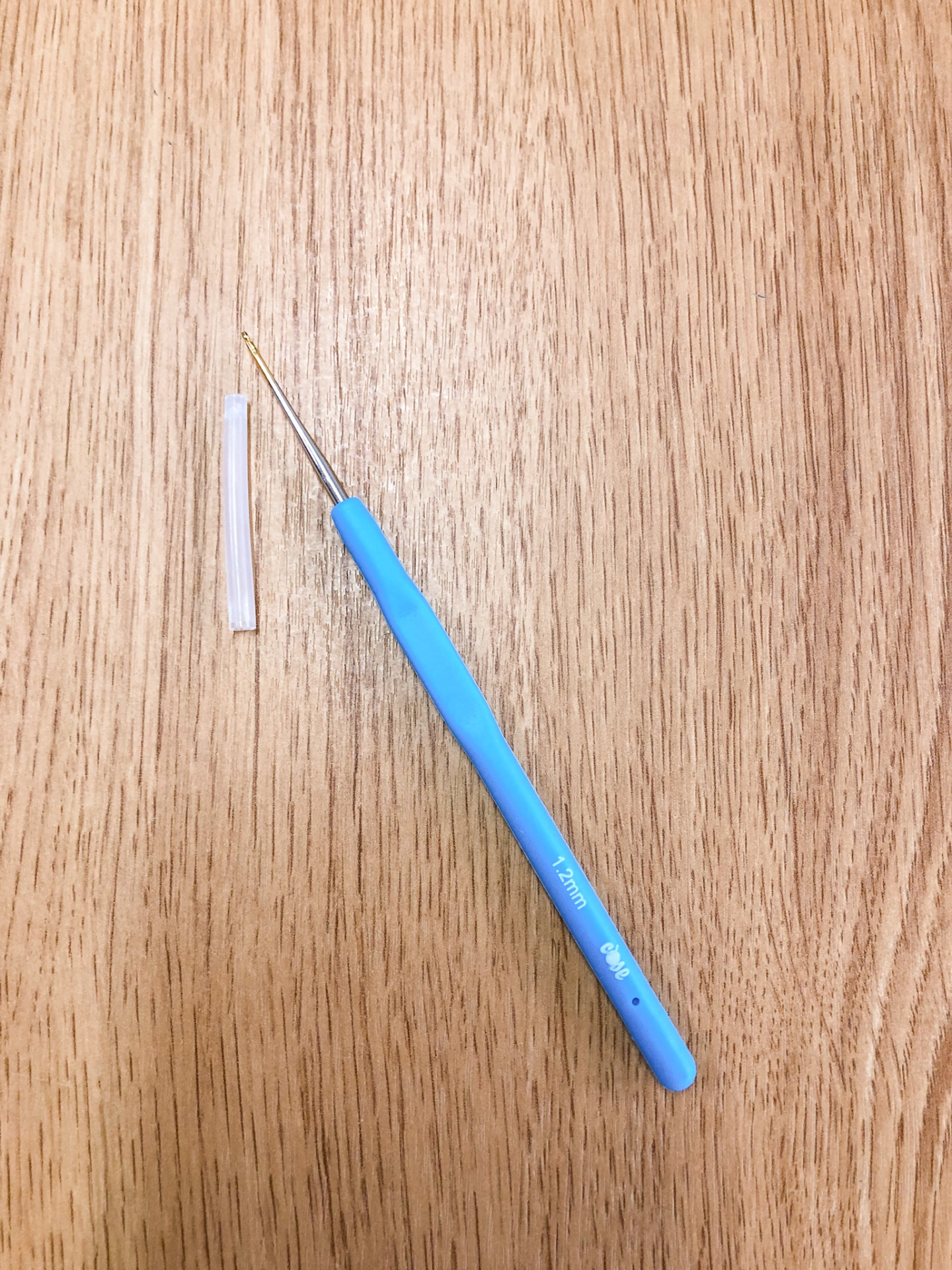 Agulha de crochê azul com cabo e ponta dourada sobre superfície de madeira clara