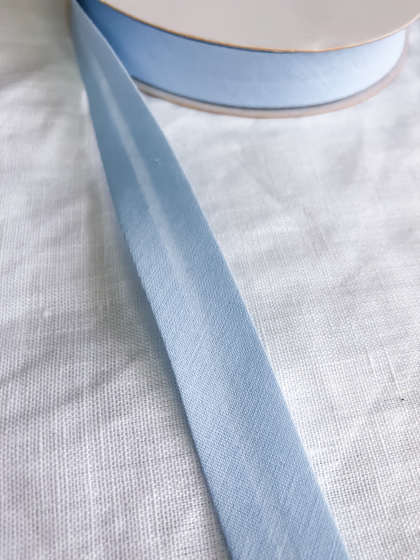Fita de tecido azul claro enrolada em carretel sobre tecido branco