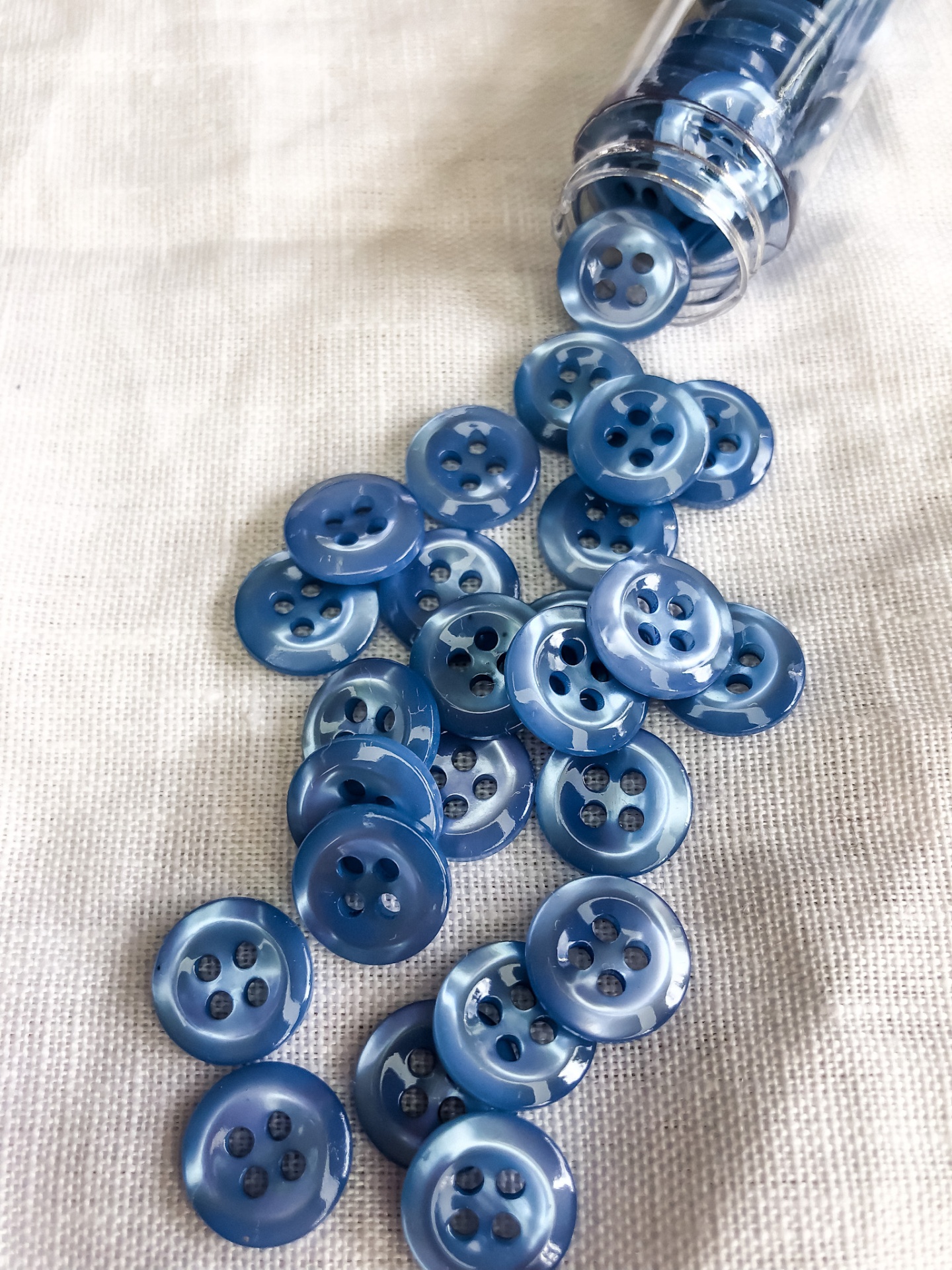 Botões azuis de plástico brilhante espalhados sobre tela bege