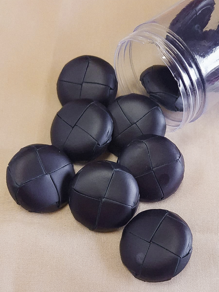 Bolas decorativas pretas de material trançado ao lado de um recipiente cilíndrico transparente