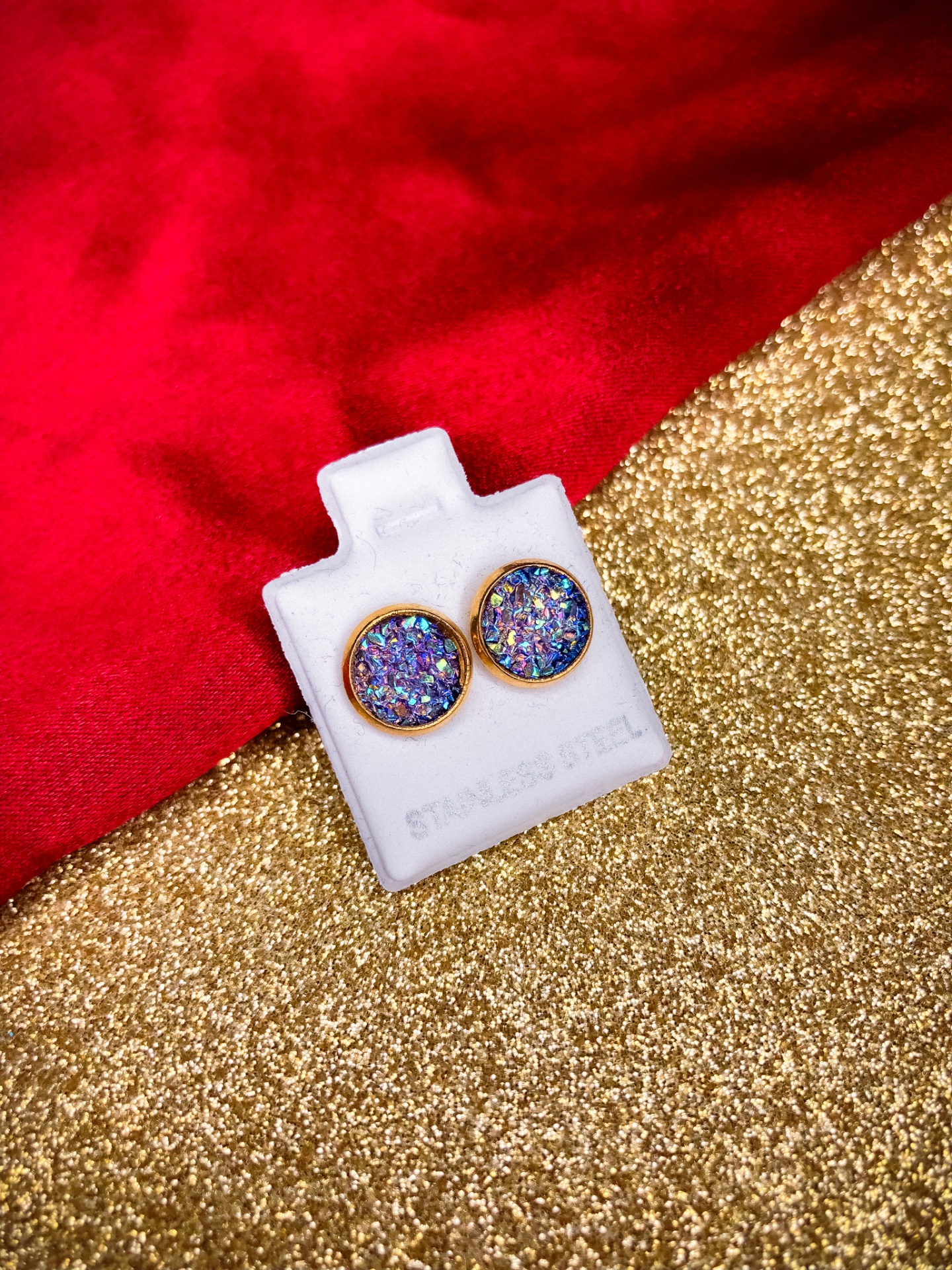 Brincos redondos dourados com padrão multicolorido num suporte branco