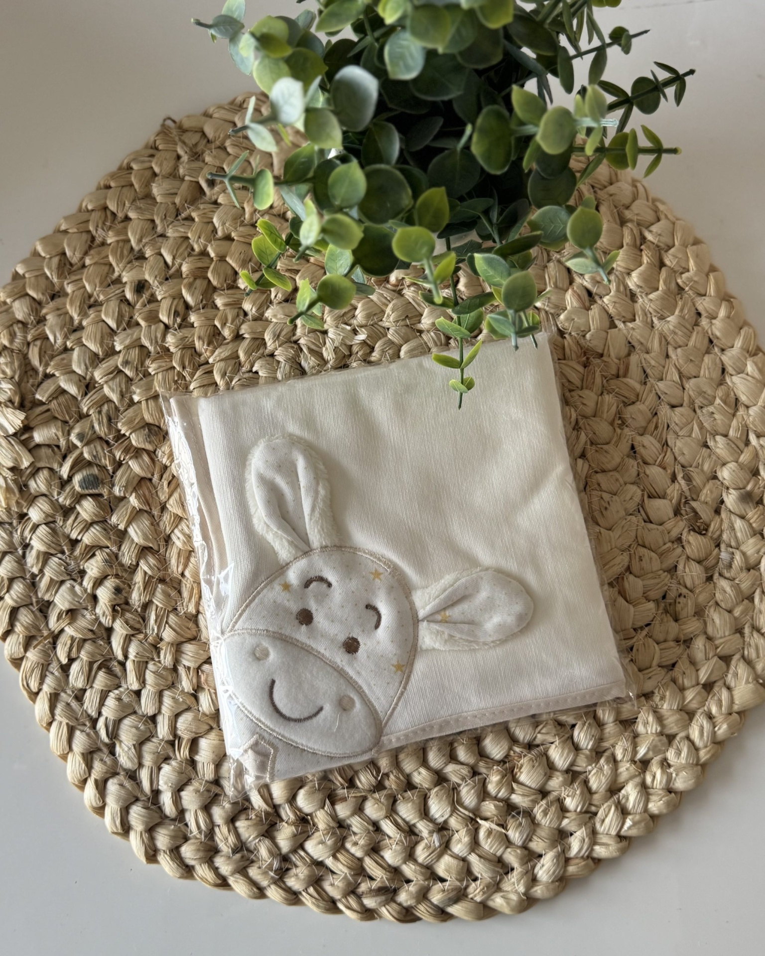 Guardanapo branco bordado com rosto de coelho sobre base trançada com planta verde