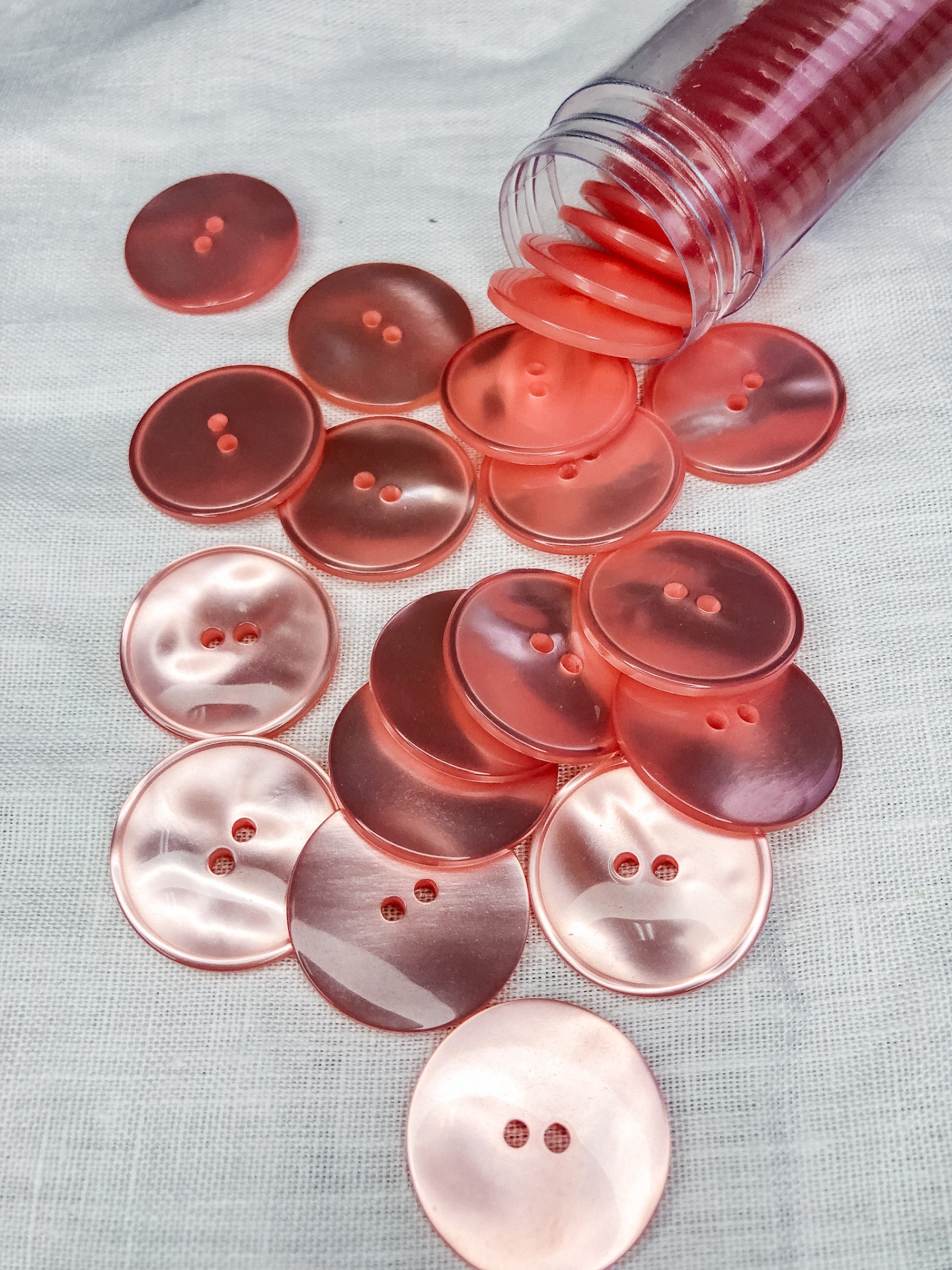 Botões rosados transparentes com dois furos sobre tecido branco