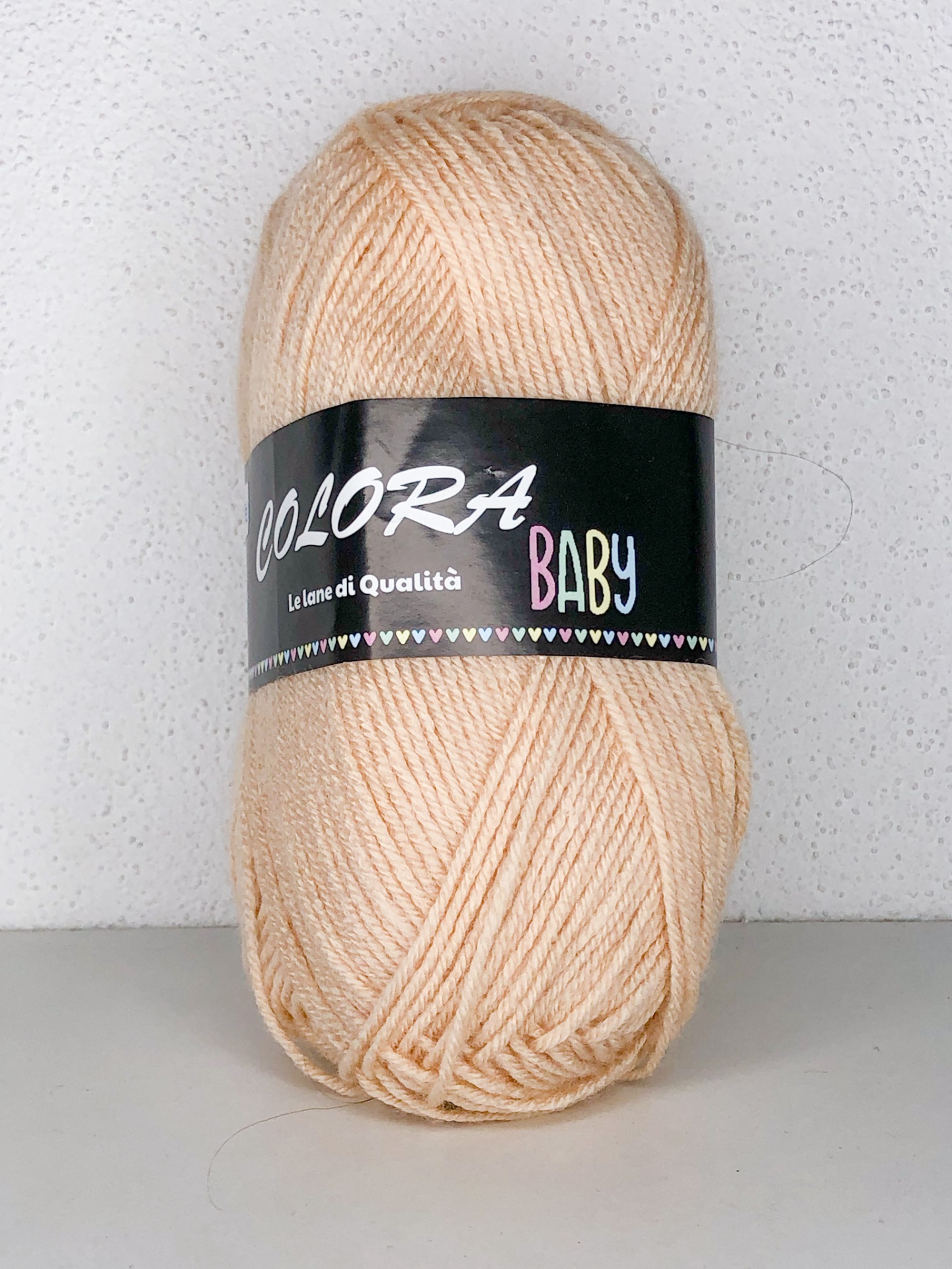 Novelo de lã bege claro com etiqueta preta escrita Colorá Baby.