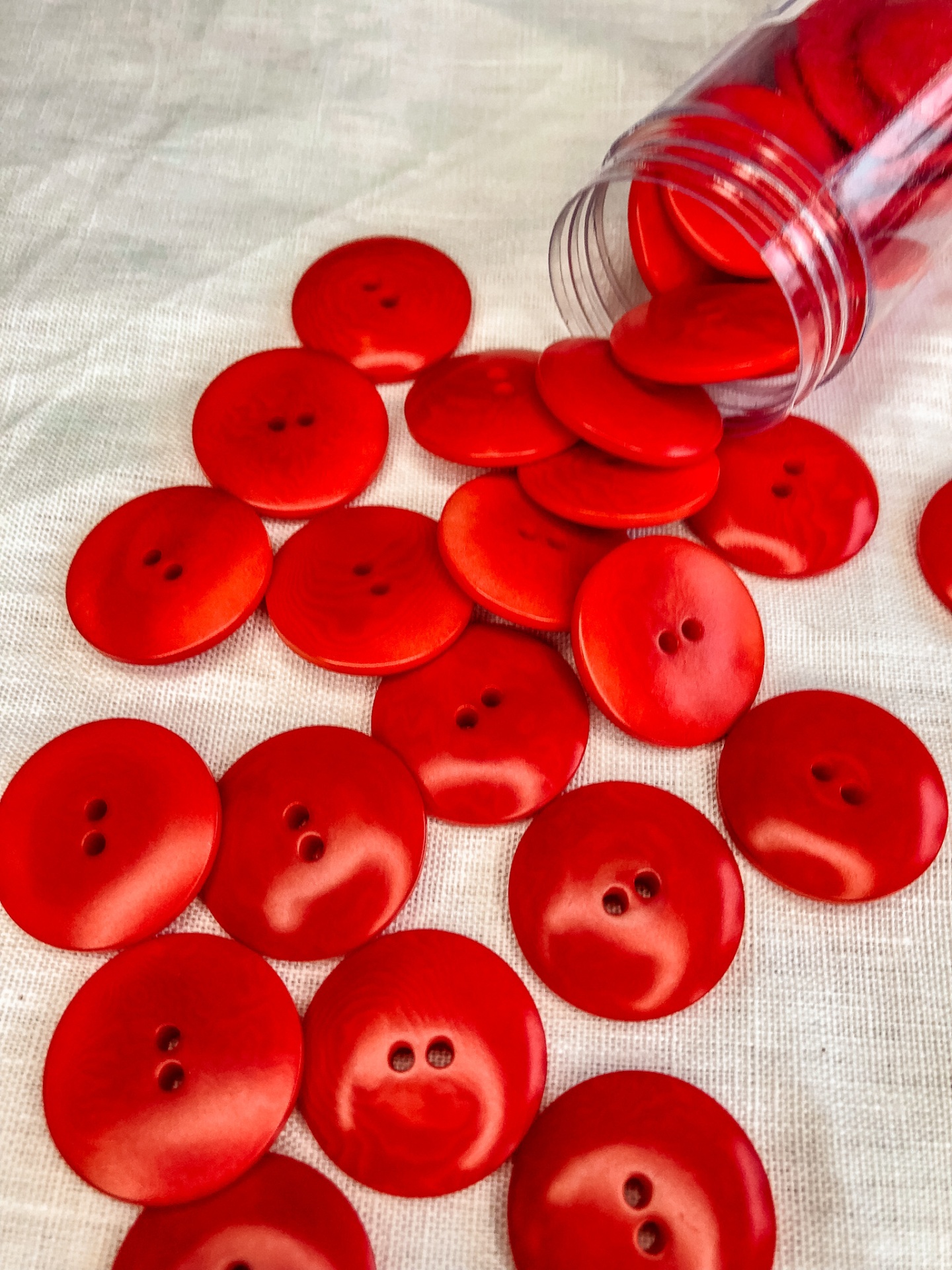 Botões vermelhos de plástico com dois furos espalhados sobre tecido branco