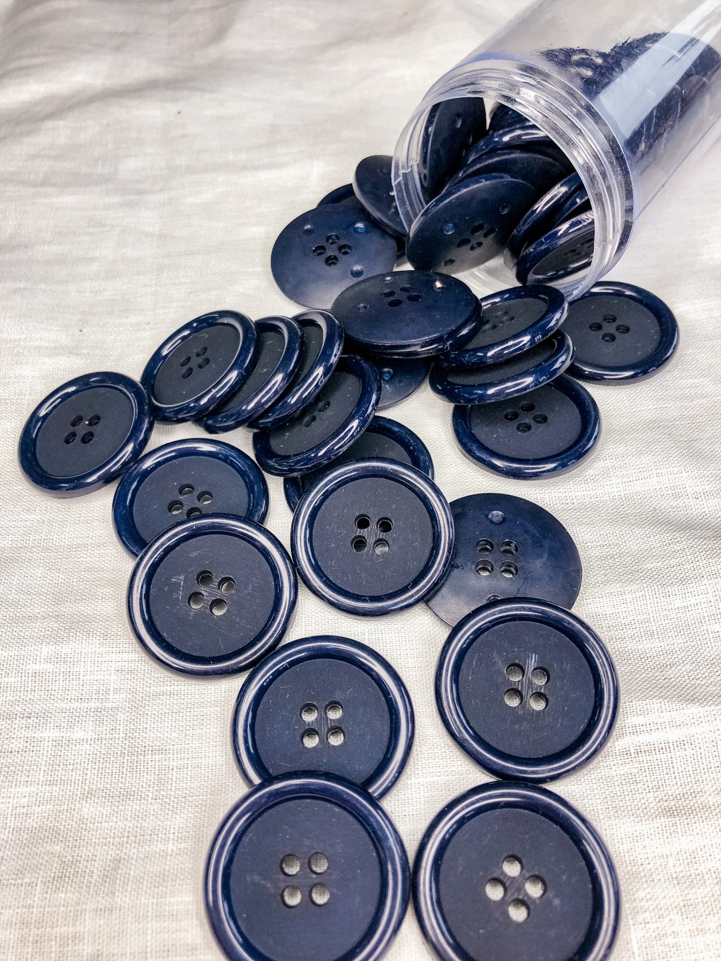 Botões azuis escuros redondos com quatro furos sobre pano branco