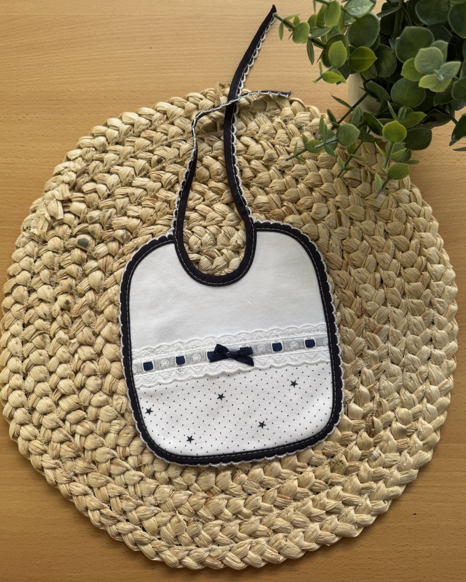 Babete de bebé branco com detalhes azuis sobre tapete de fibras naturais