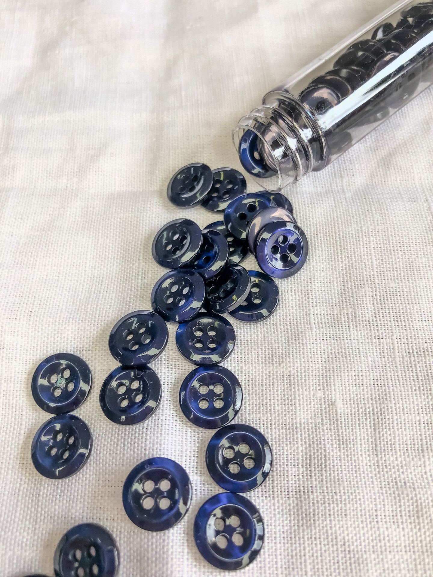 Botões azuis brilhantes com quatro orifícios num tecido branco, parcialmente dentro de um frasco transparente