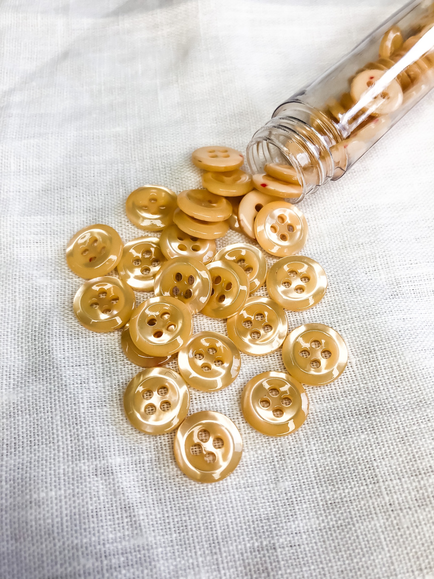 Botões bege de plástico com quatro furos sobre tecido branco e em frasco transparente aberto