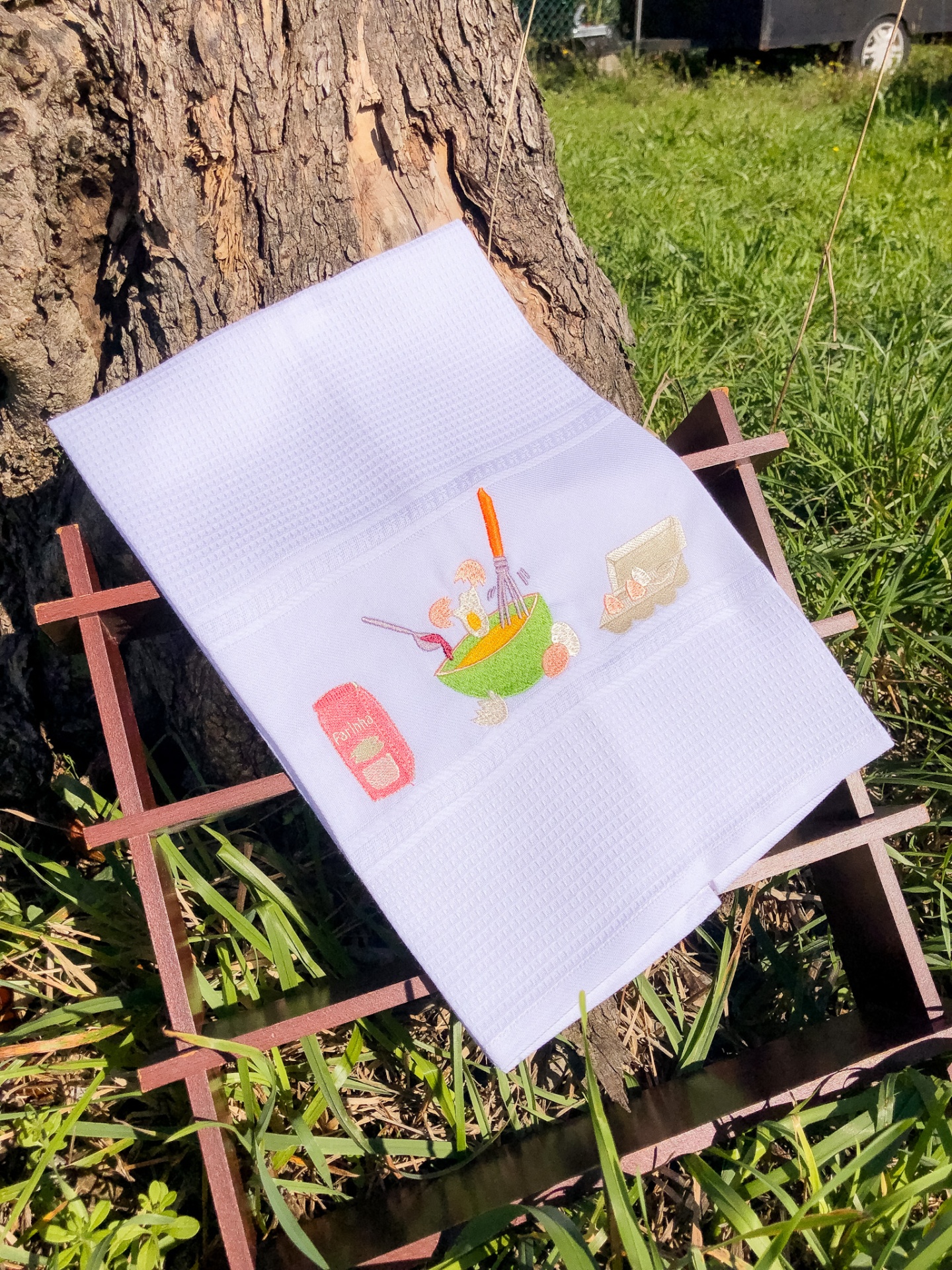 Toalha branca com bordado colorido disposta sobre estrutura de madeira em ambiente exterior