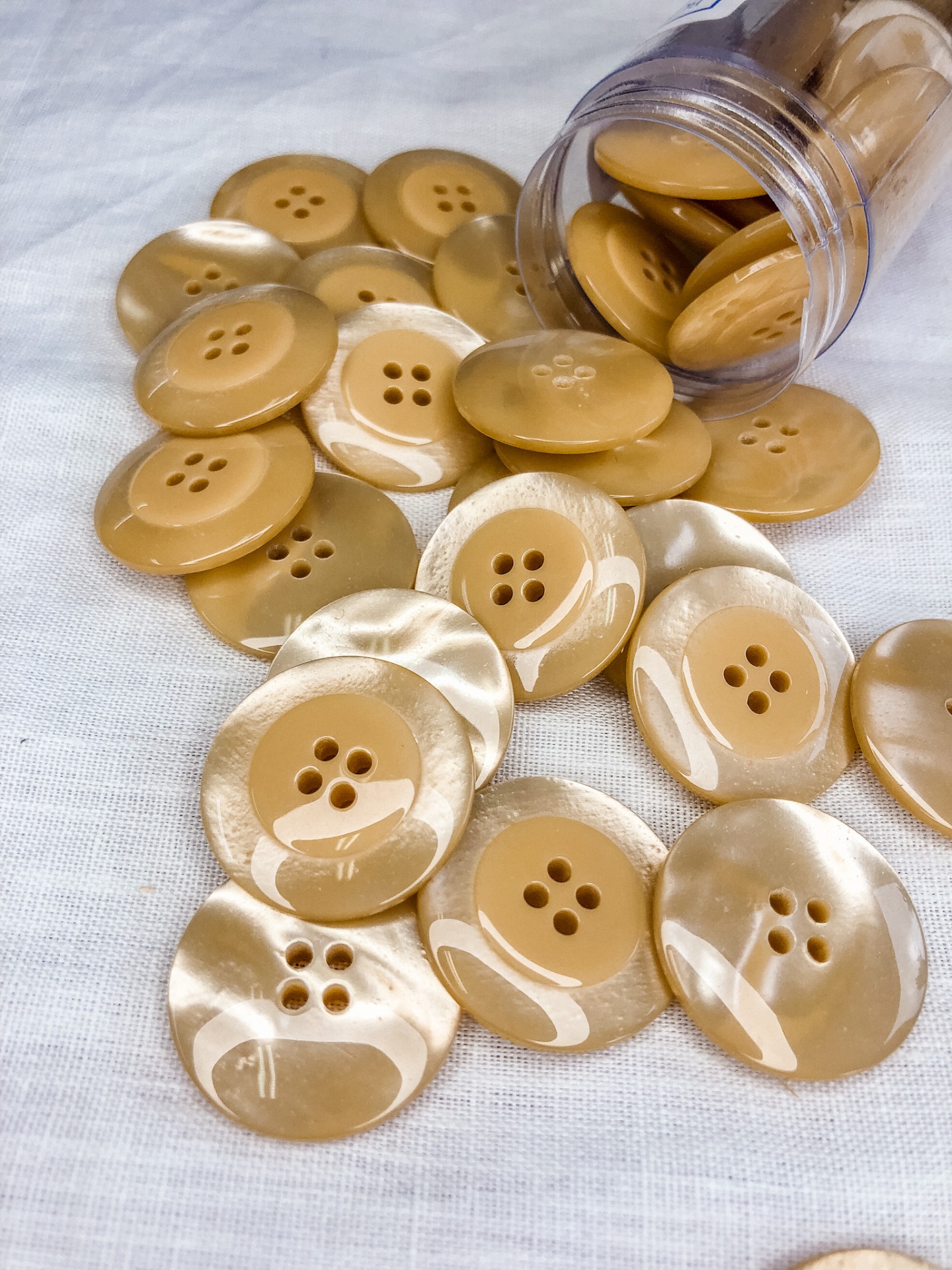 Botões castanhos claros com quatro furos em tecido branco, alguns marmoreados, com frasco transparente