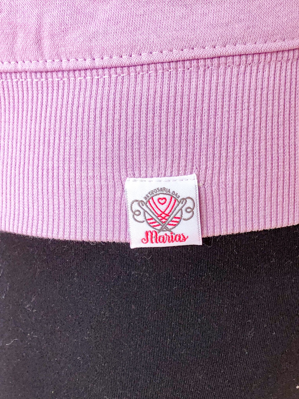 Etiqueta de peça de vestuário rosa com texto Retrosaria Olis e Marias