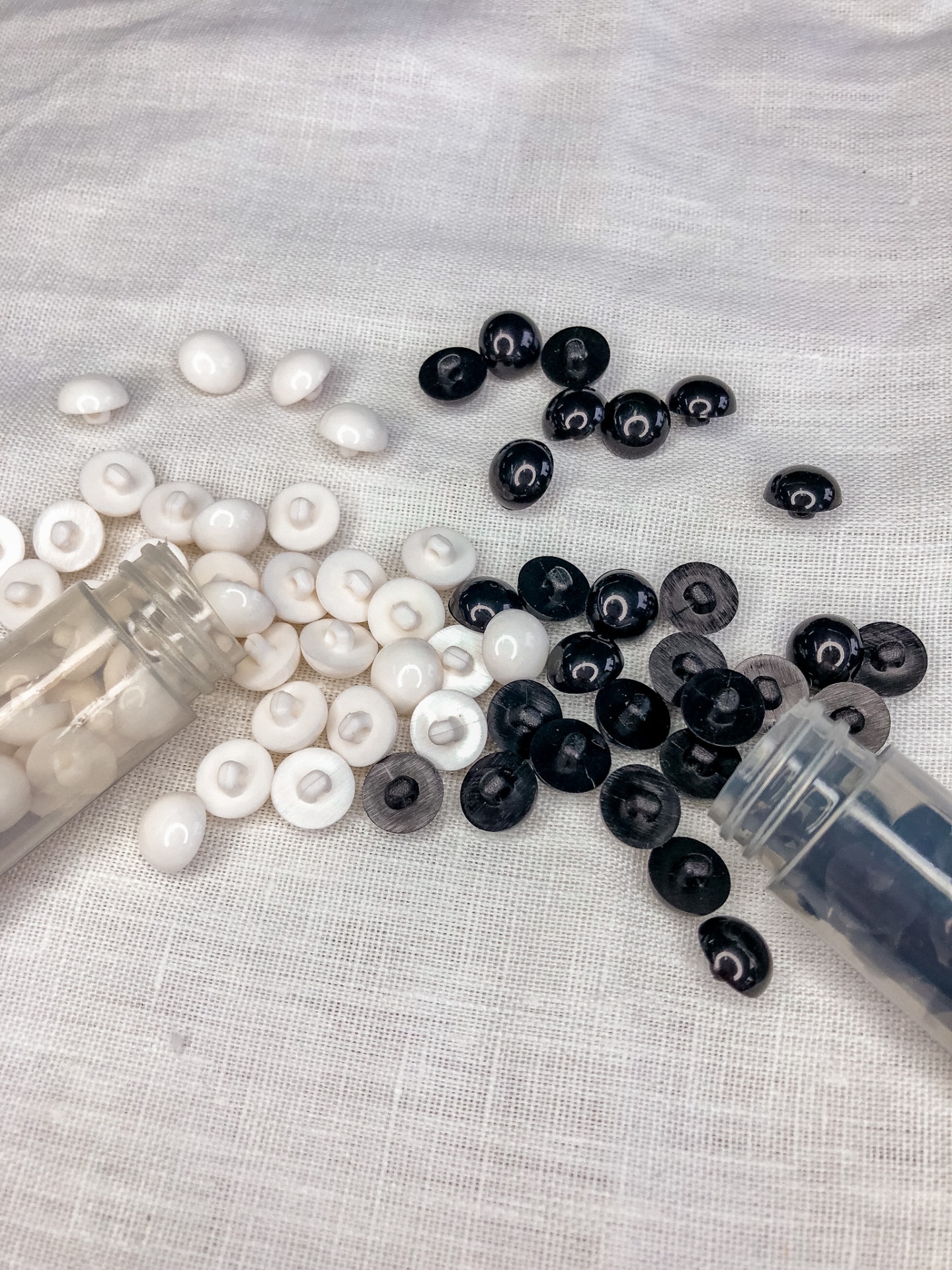 Botões brancos e pretos pequenos em tecido claro com recipientes plásticos