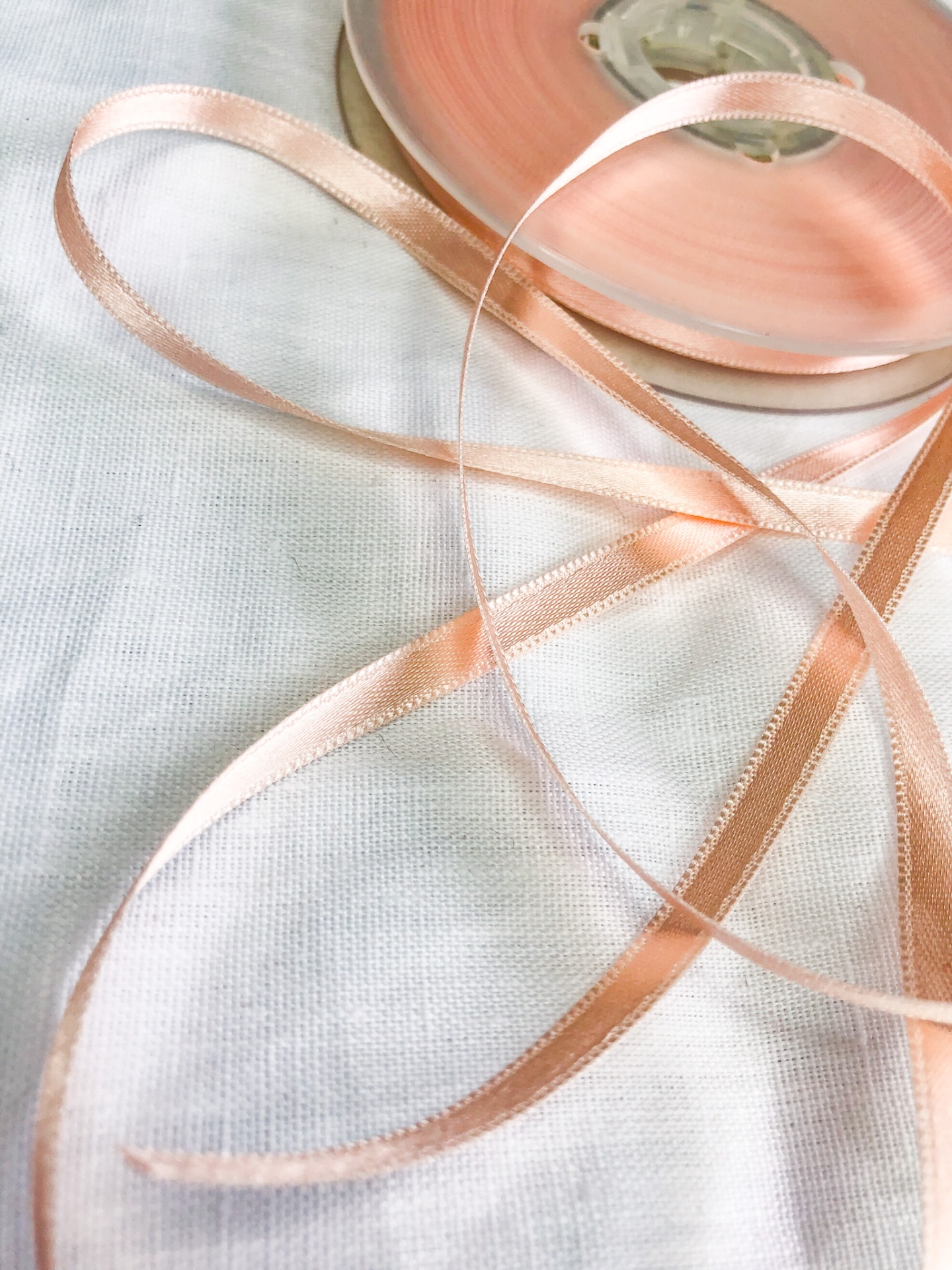 Fita de cetim cor de pêssego desenrolada sobre tecido branco