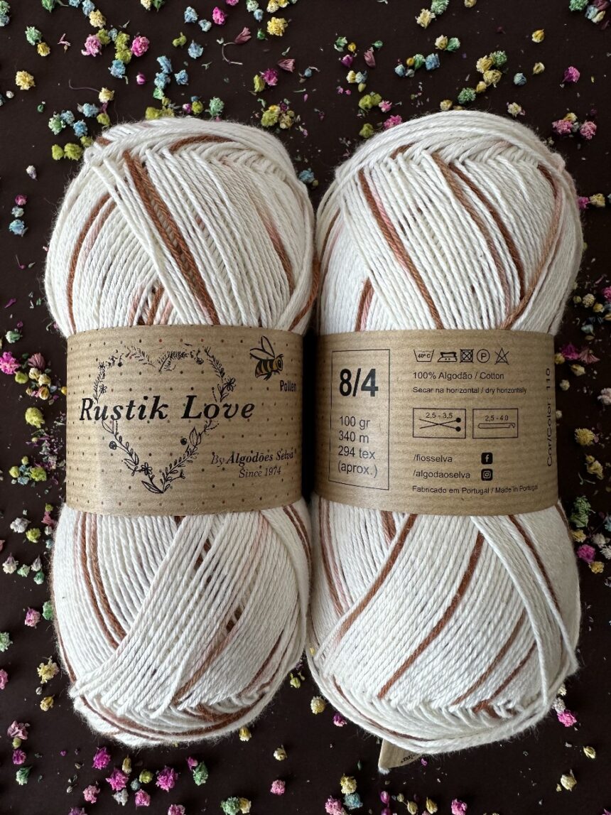 Novelos de fio Rustik Love algodão branco com riscas castanhas em superfície escura com flores coloridas