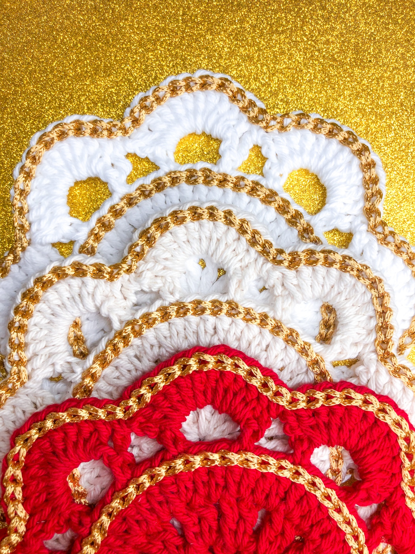 Peças de croché em branco e vermelho com fio dourado em fundo dourado brillante.