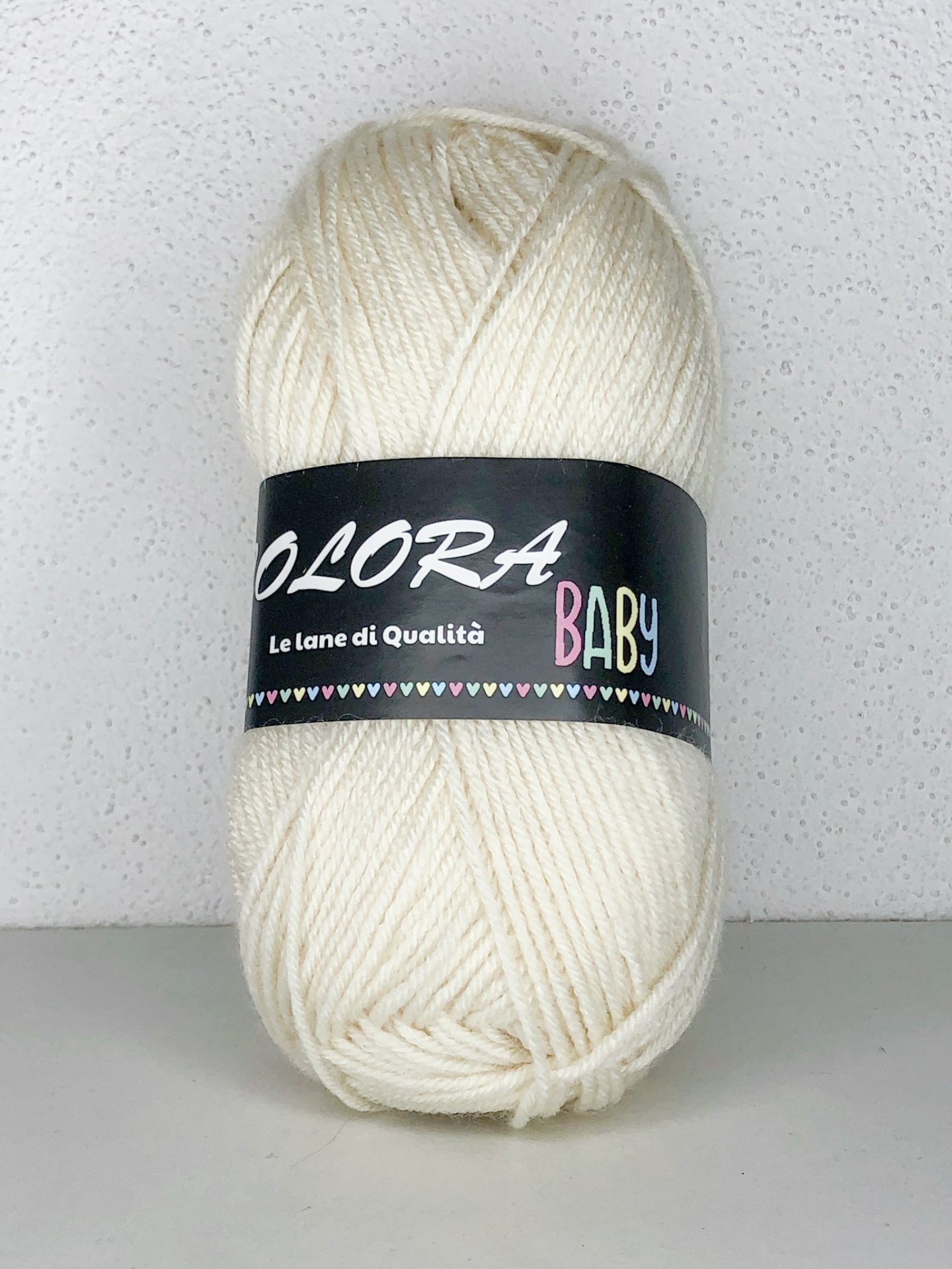 Novelo de lã creme com etiqueta preta, texto OLORA BABY, em fundo branco.