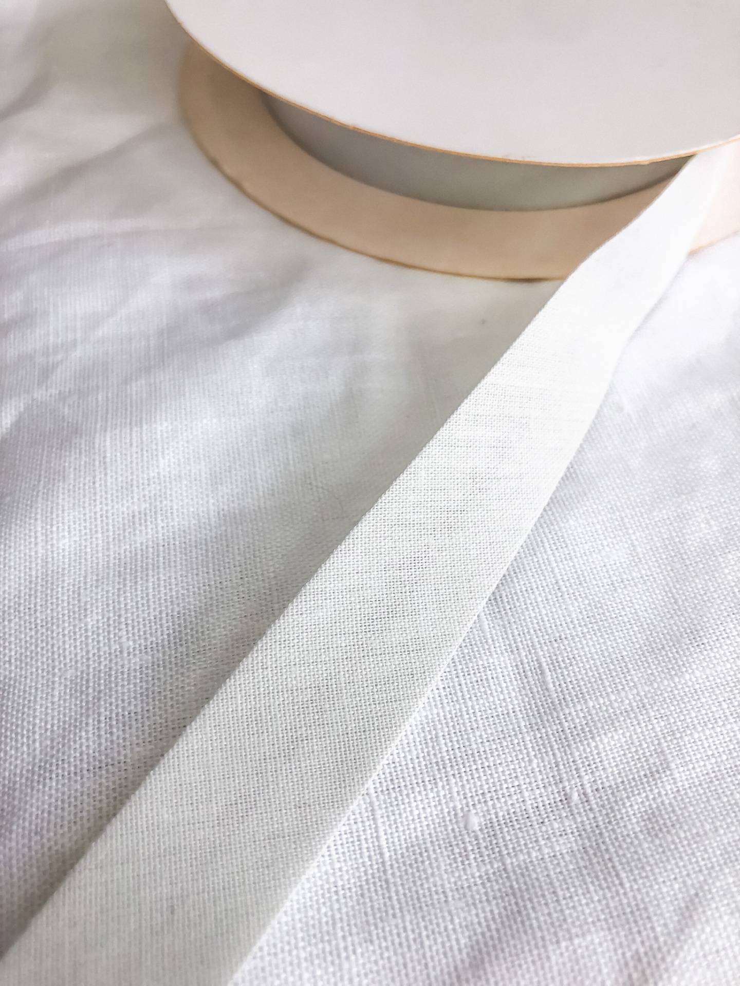 Fita de tecido branca sobre carretel cor de bege em pano branco