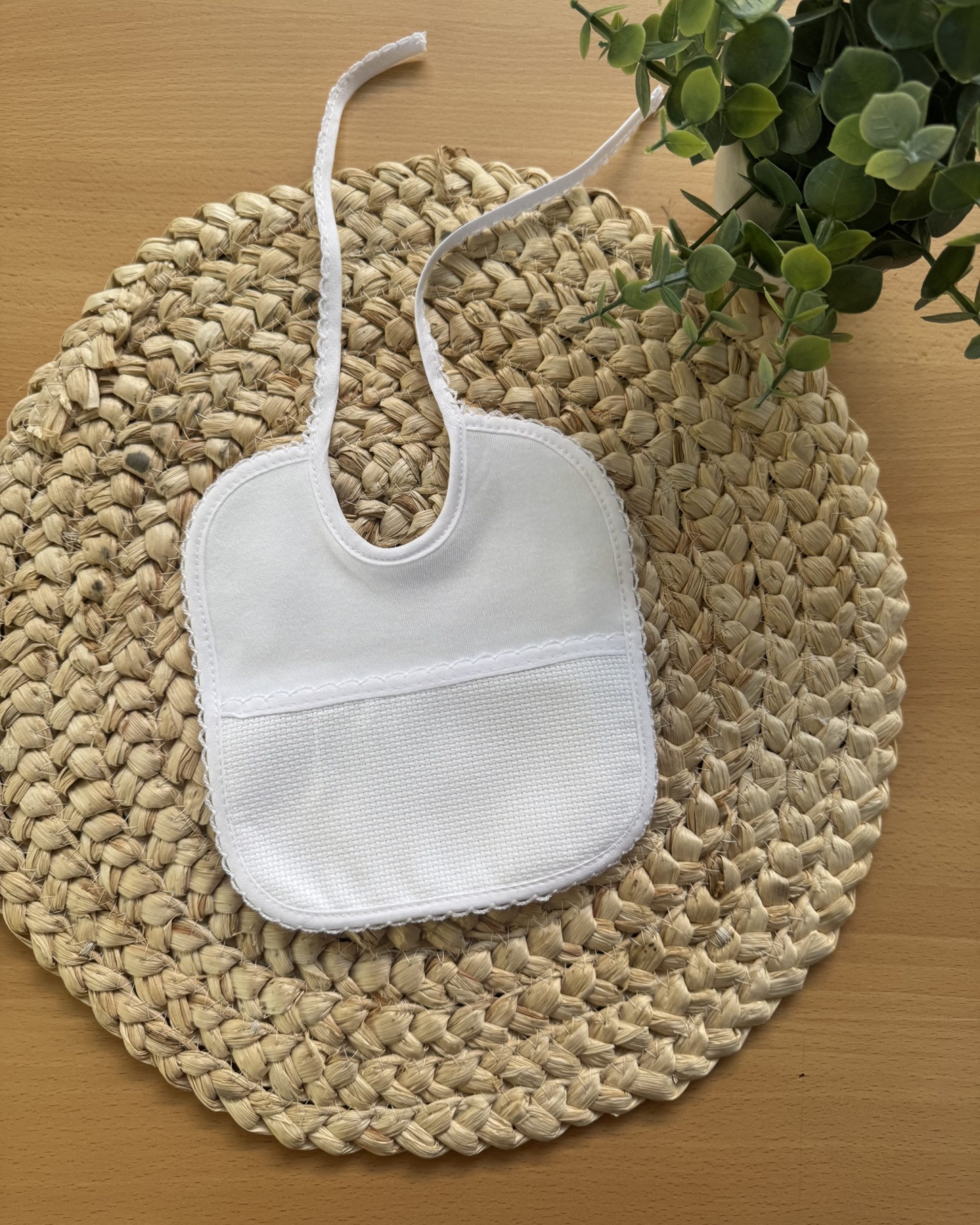Babete branco de bebé com bolso sobre tapete de fibras naturais e planta verde