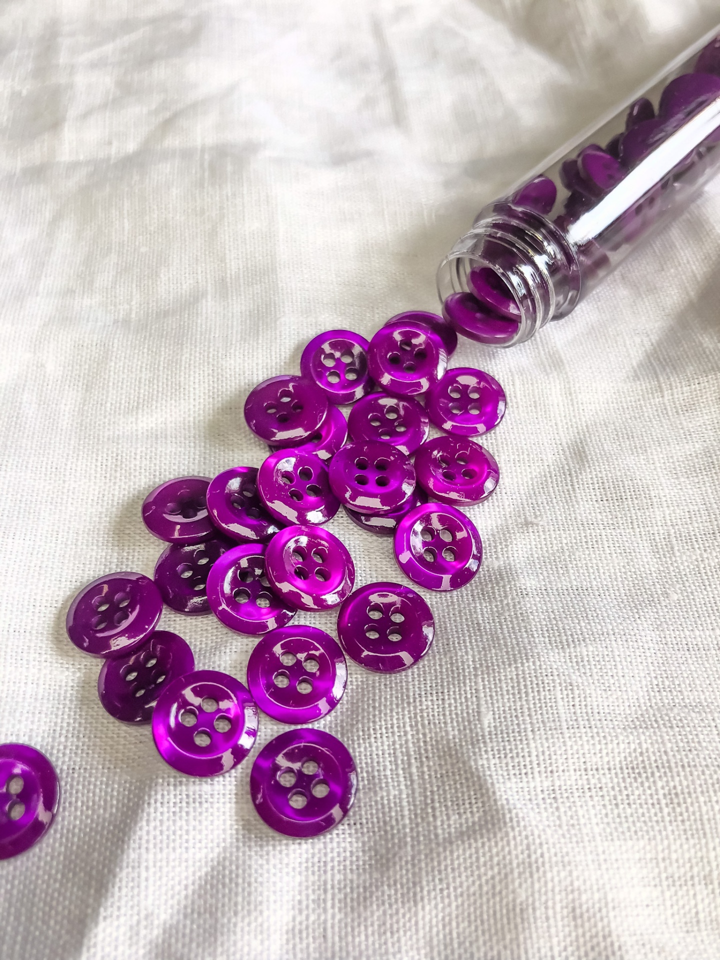 Botões pequenos roxos brilhantes sobre tecido branco com frasco transparente aberto