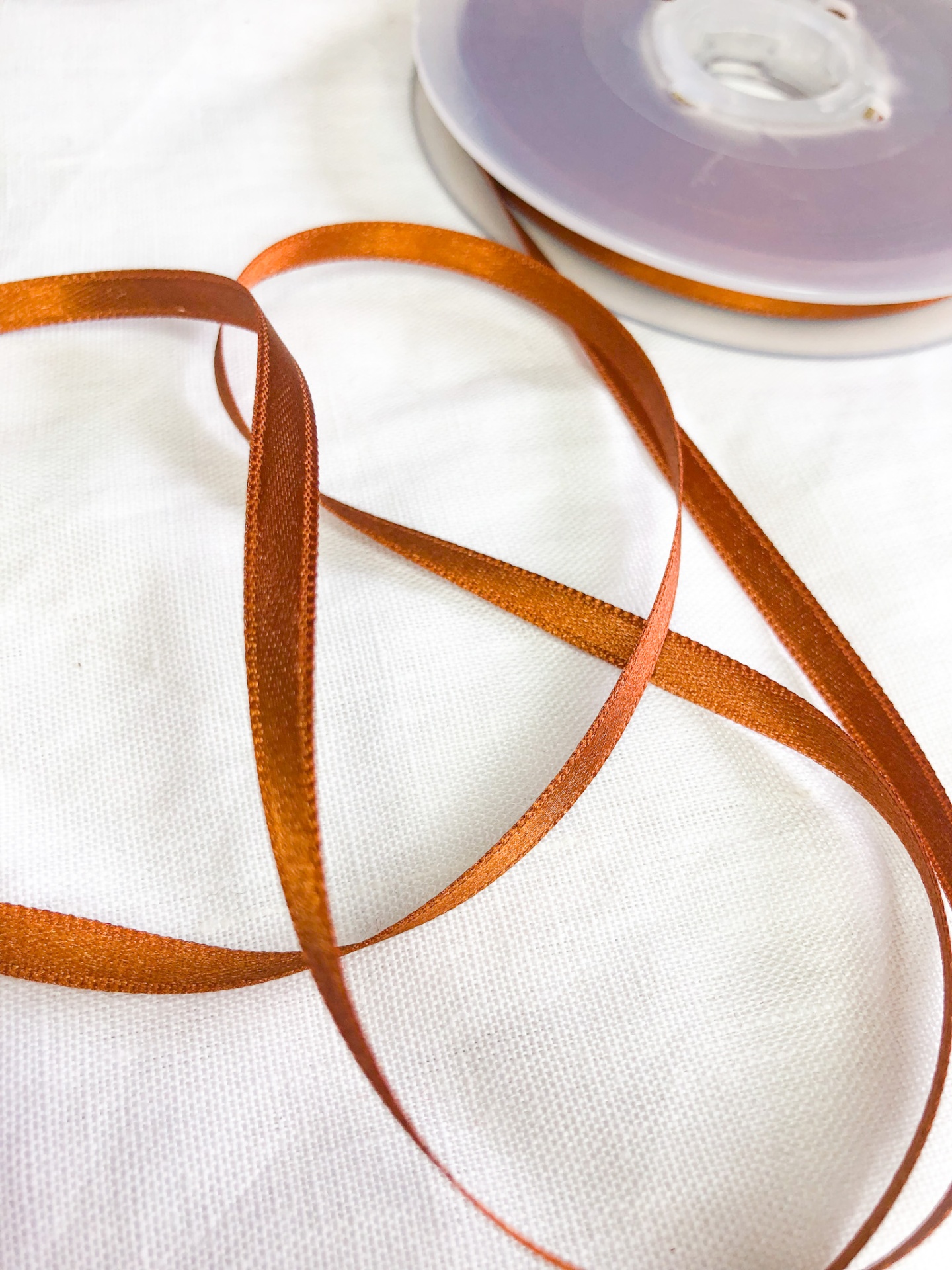 Fita de cetim laranja queimado em rolo sobre tecido branco