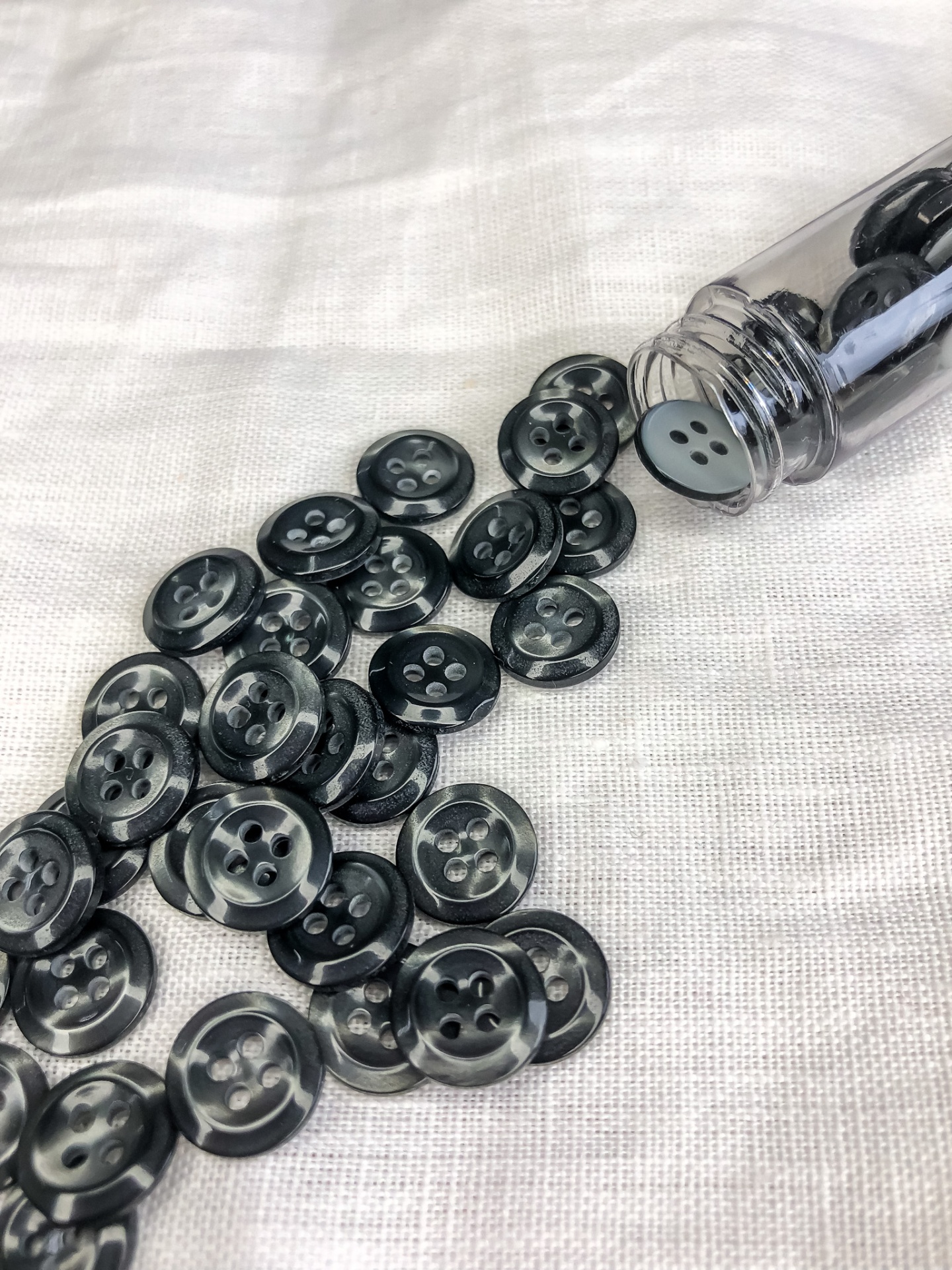 Botões pretos redondos com 4 furos em plástico brilhante sobre tecido branco e frasco de vidro